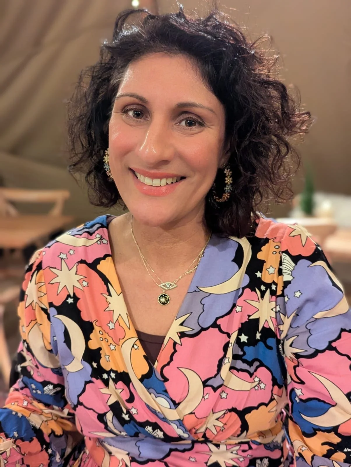 Sonia our yoga teacher, curly hair, colorful patterned blouse, and gold jewelry.