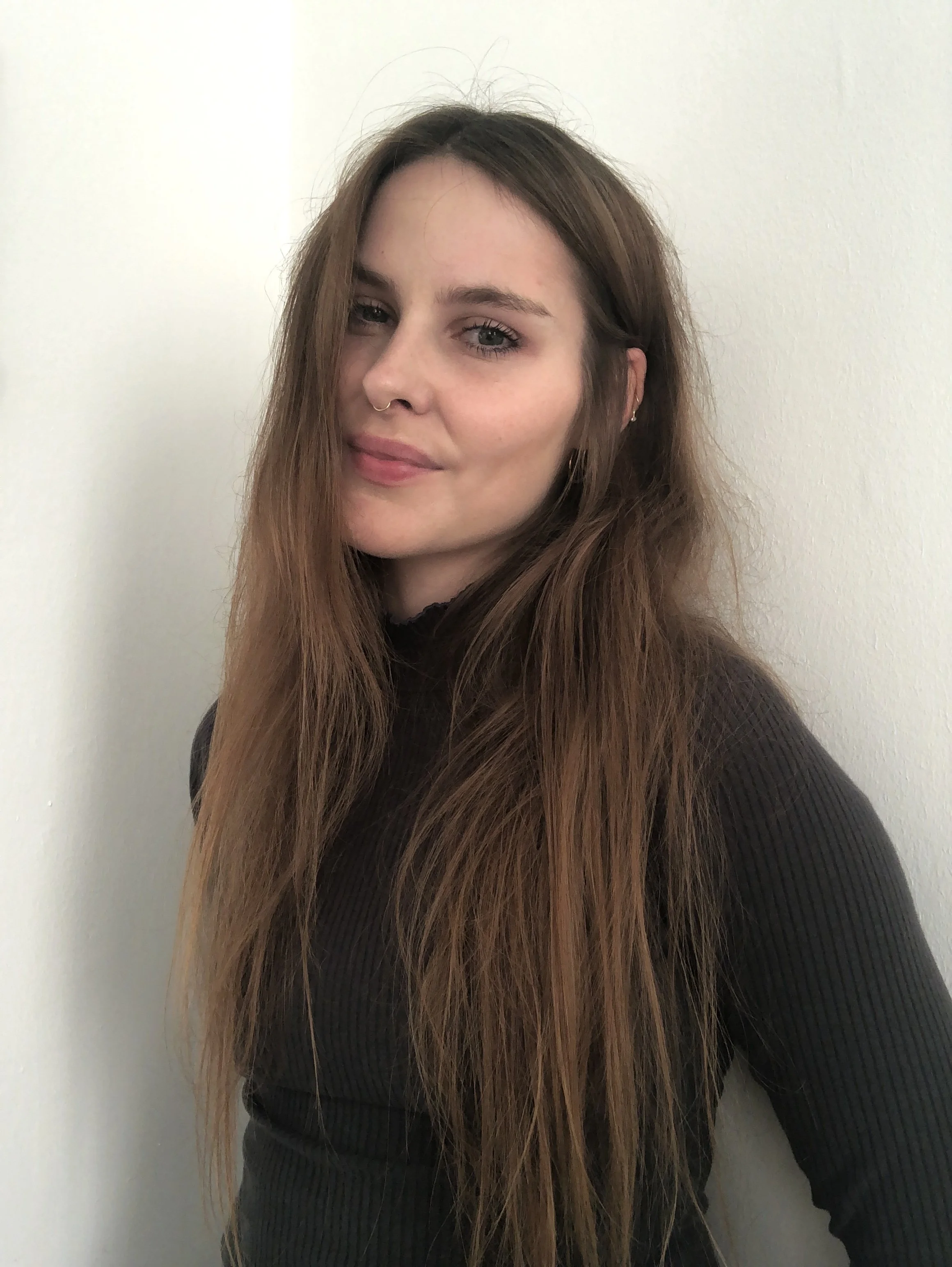 Woman with long brown hair wearing a black top against a white background.