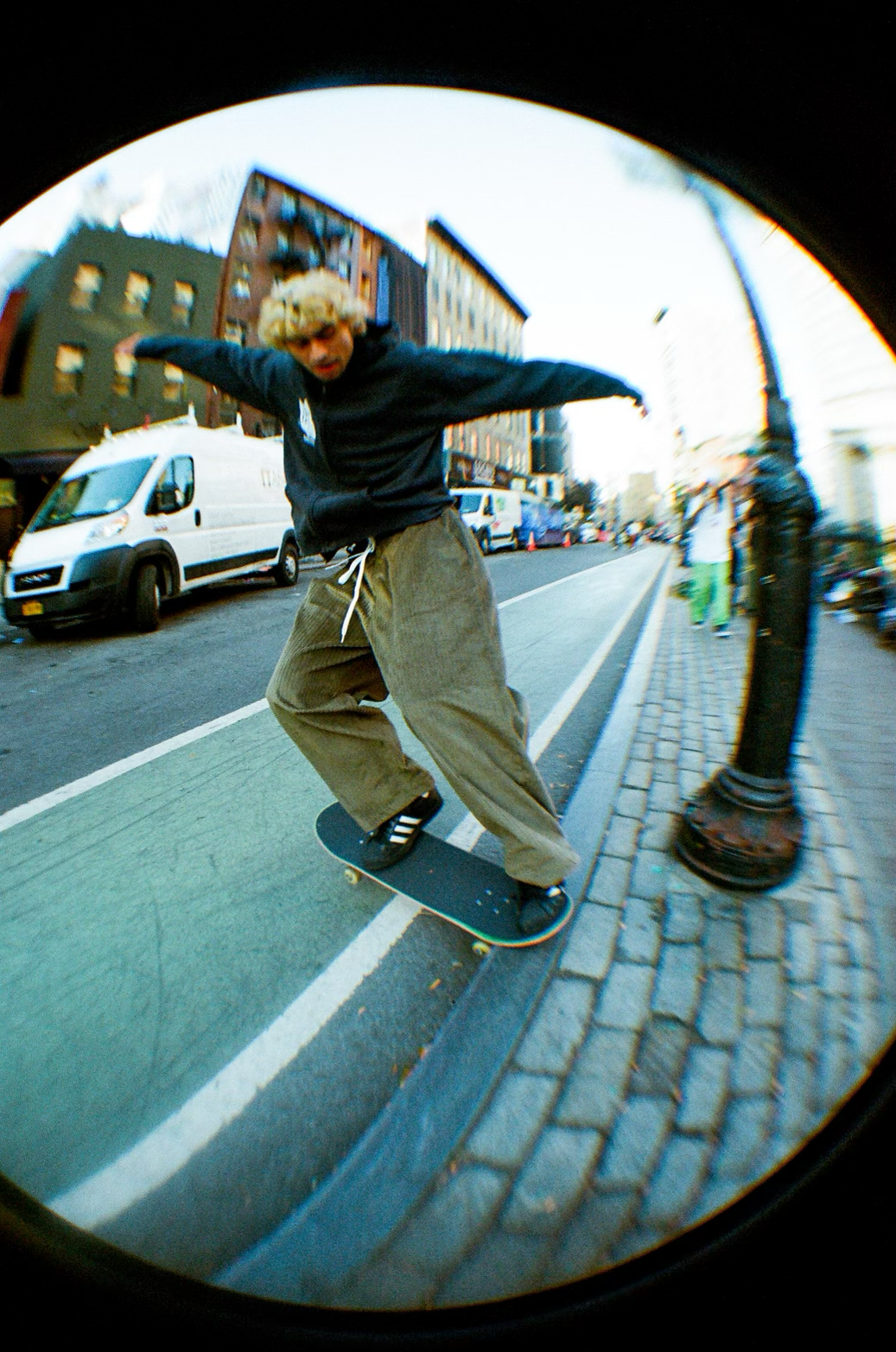 Skateboarder performing a trick on a city street, seen through a fisheye lens.