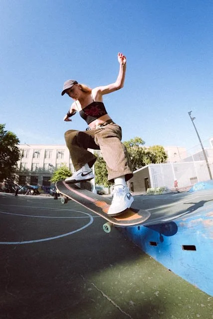 Person skateboarding on a park basketball court with a blue sky background.