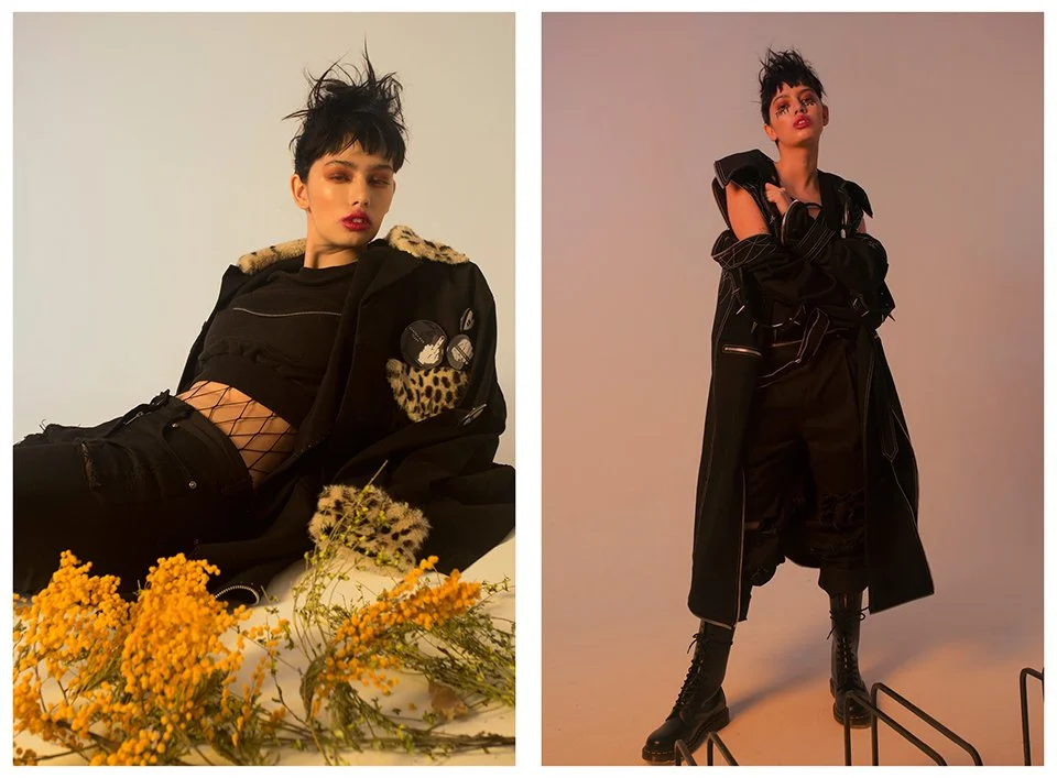 Two women posing in edgy, dark fashion outfits; one lying among yellow flowers, the other standing with arms crossed in a studio.