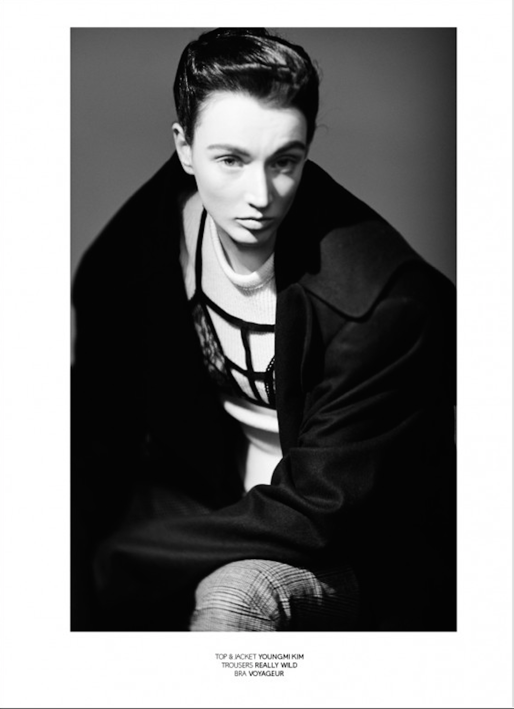 Black and white portrait of a young woman with short hair, wearing a top, jacket, and patterned trousers, looking directly at the camera.