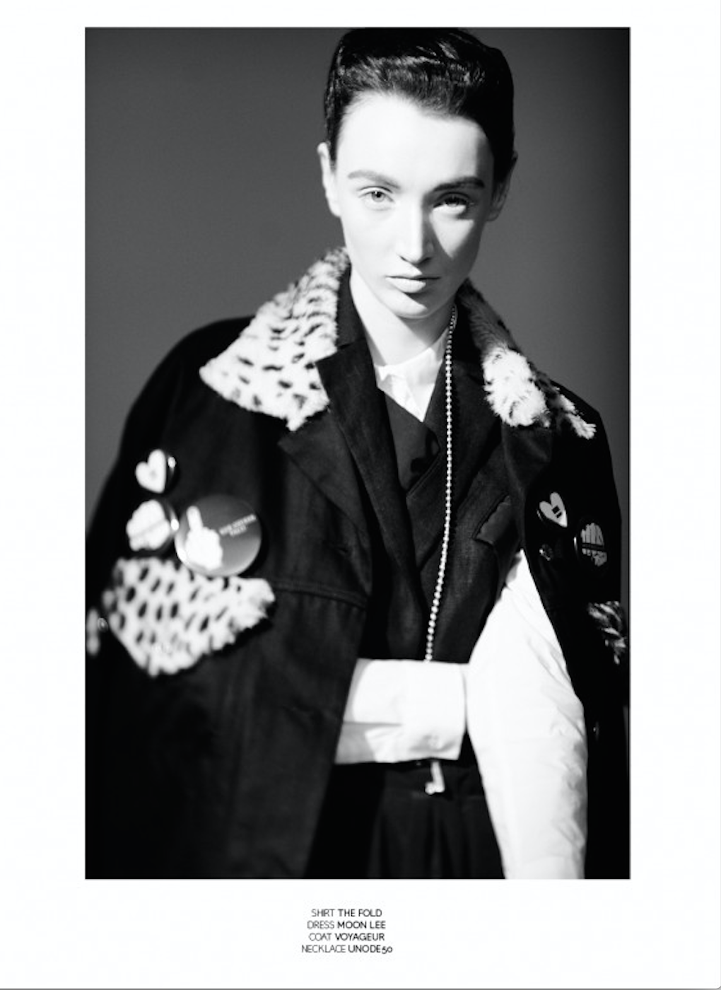 Black and white fashion portrait of a woman wearing a jacket with leopard print details and pins, looking directly at the camera.