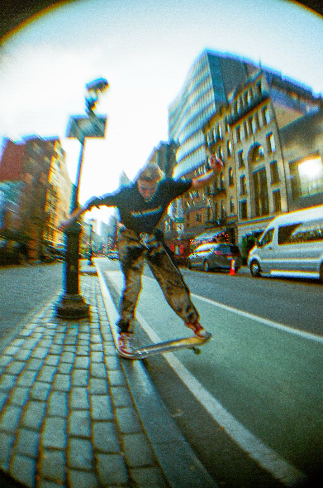 Person skateboarding on a city street with buildings and cars in the background.