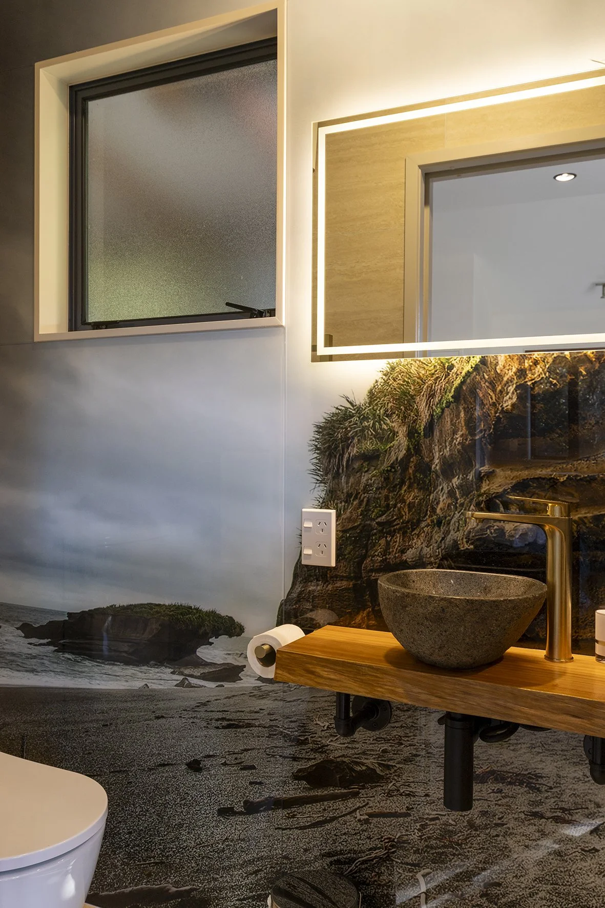 Bathroom with a nature beach mural on the wall, a wooden vanity with a stone sink, and a mirror with LED lighting.