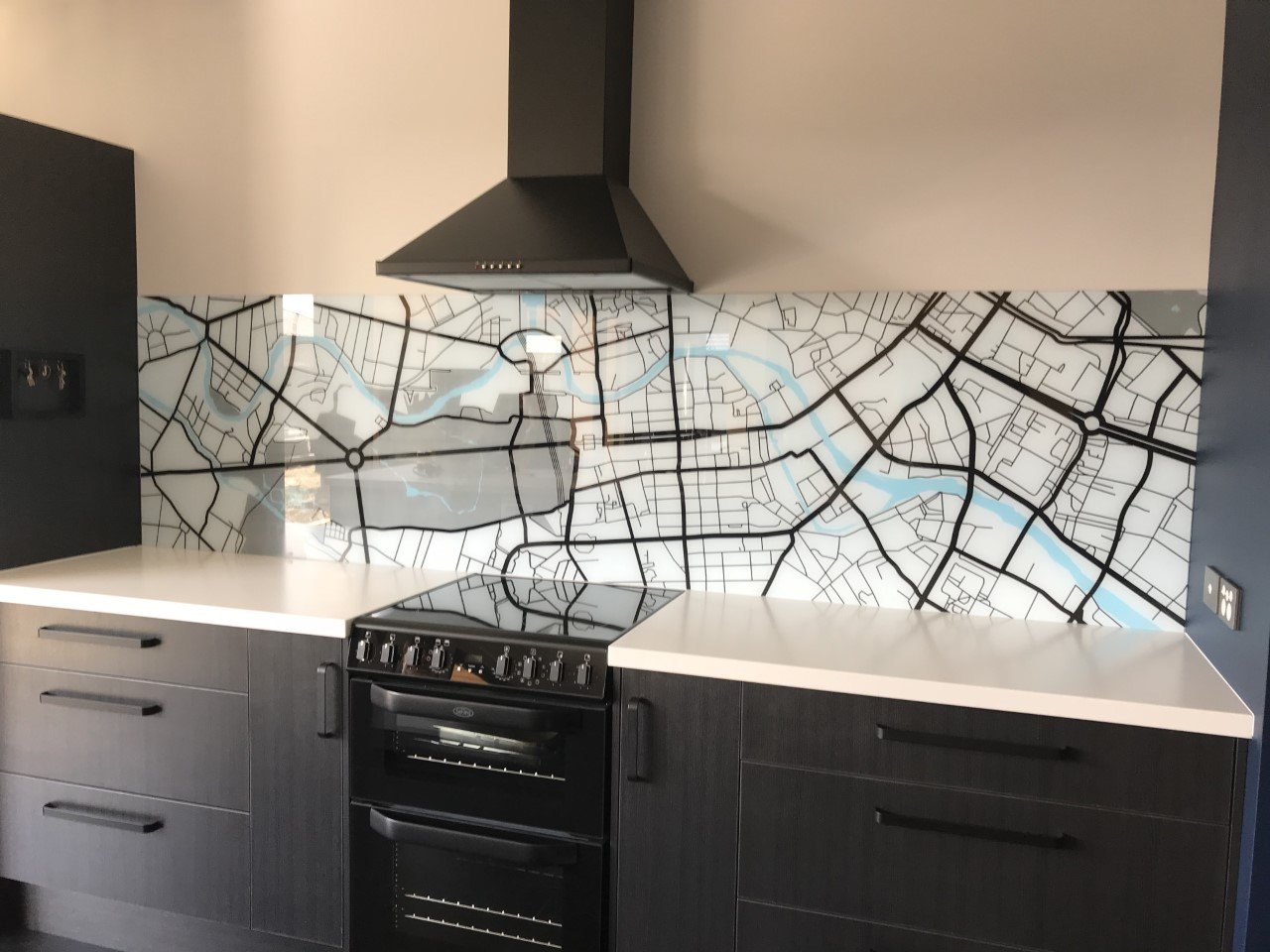 Kitchen with black cabinets, white countertops, and a map-themed glass backsplash.