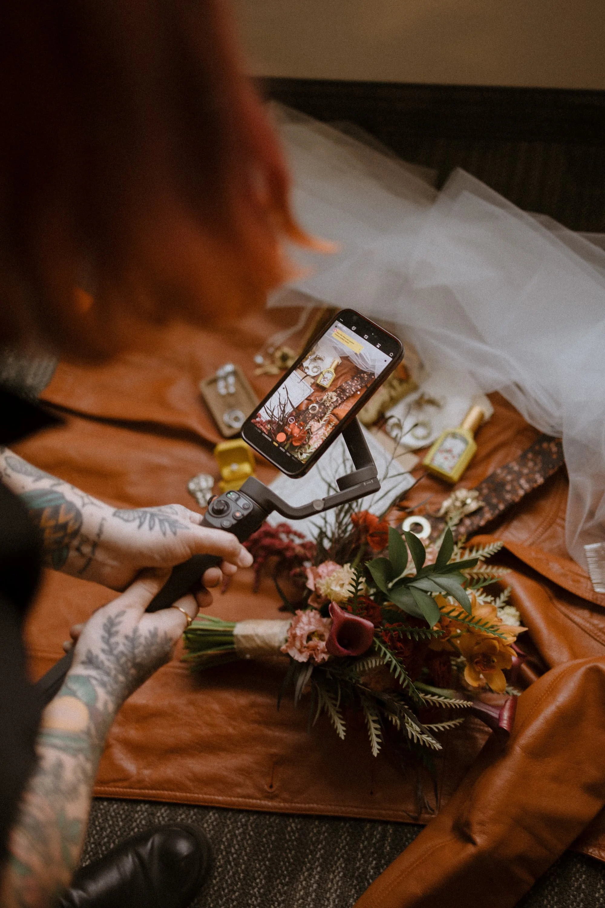 Holly holds a gimbal with her phone and films a flatlay including wedding invitations, a bouquet, rings, and other small detail items.