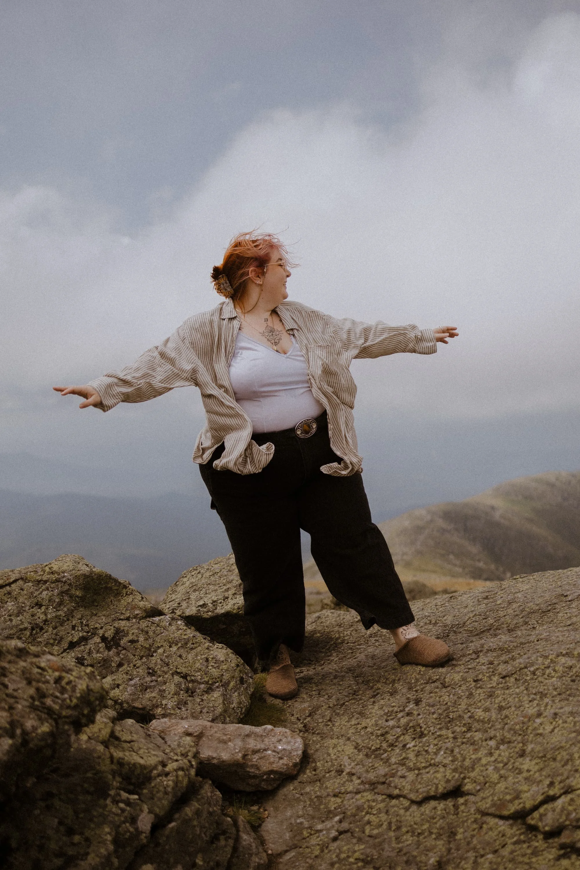 Alyssa stands on Mt. Washington with their arms spread wide. A cloud floats behind her head.