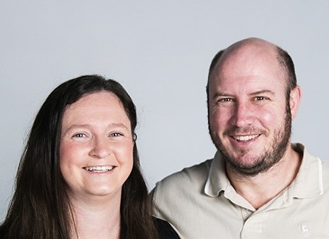 A man and woman smiling together against a light background.