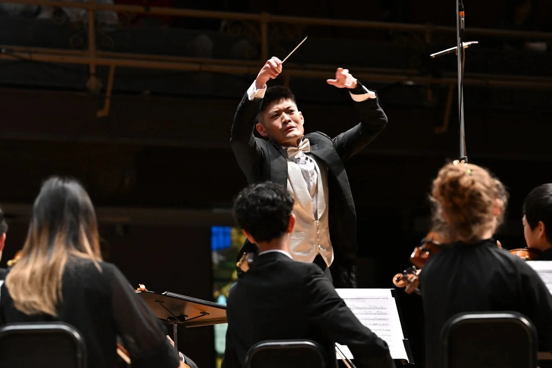 Conductor in a tuxedo leading an orchestra during a performance.