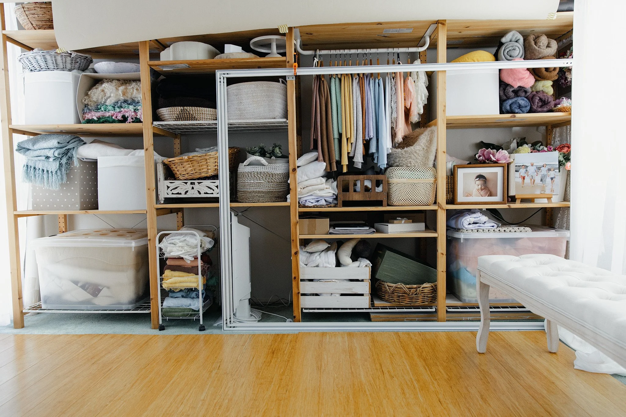 Sydney newborn studio with a large wooden shelving unit filled with folded clothes, laundry baskets, framed photographs, and decorative items in a room with wooden flooring.