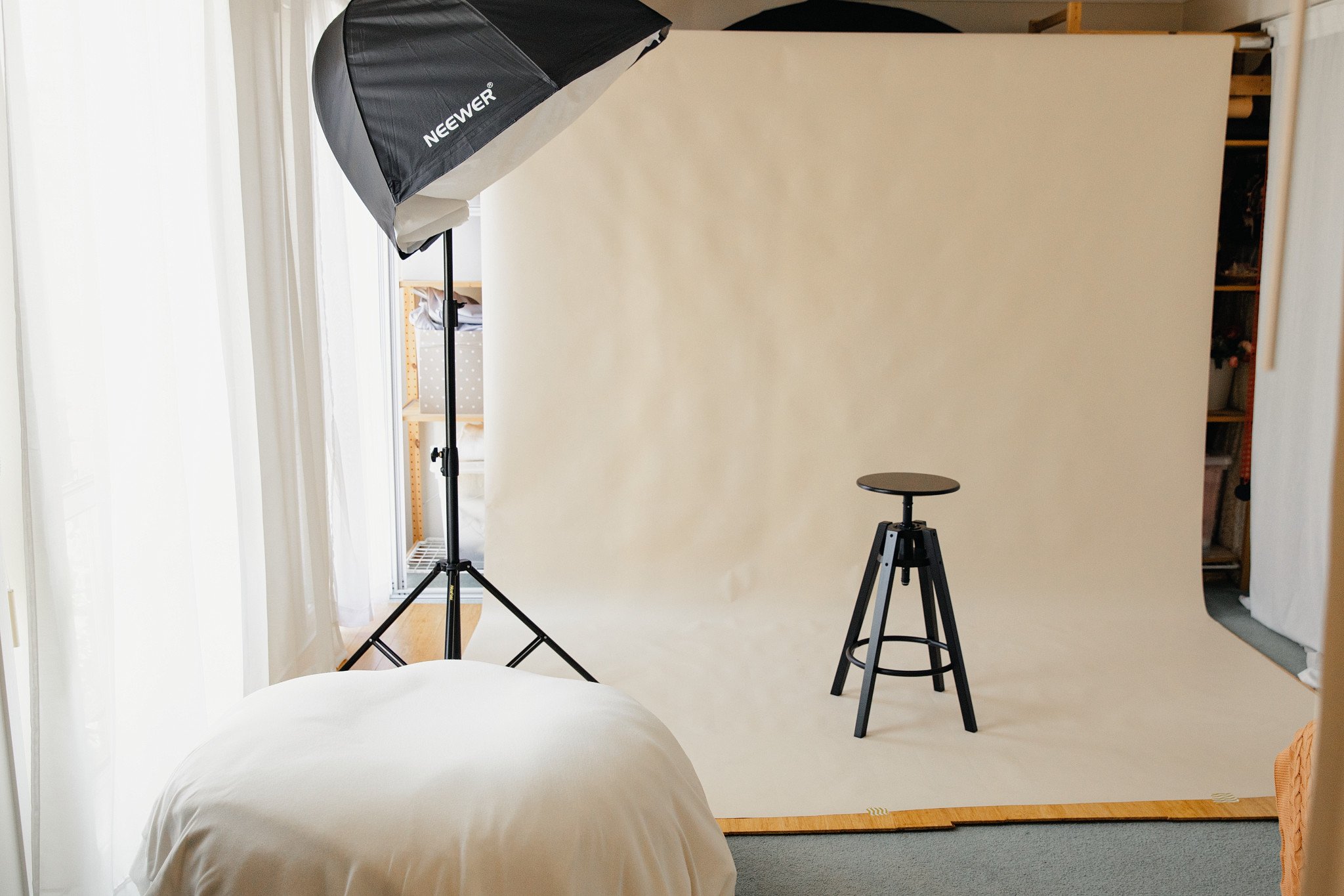 A photography studio setup with a backdrop, lighting equipment, and a stool, inside a room with a bed and a closet.