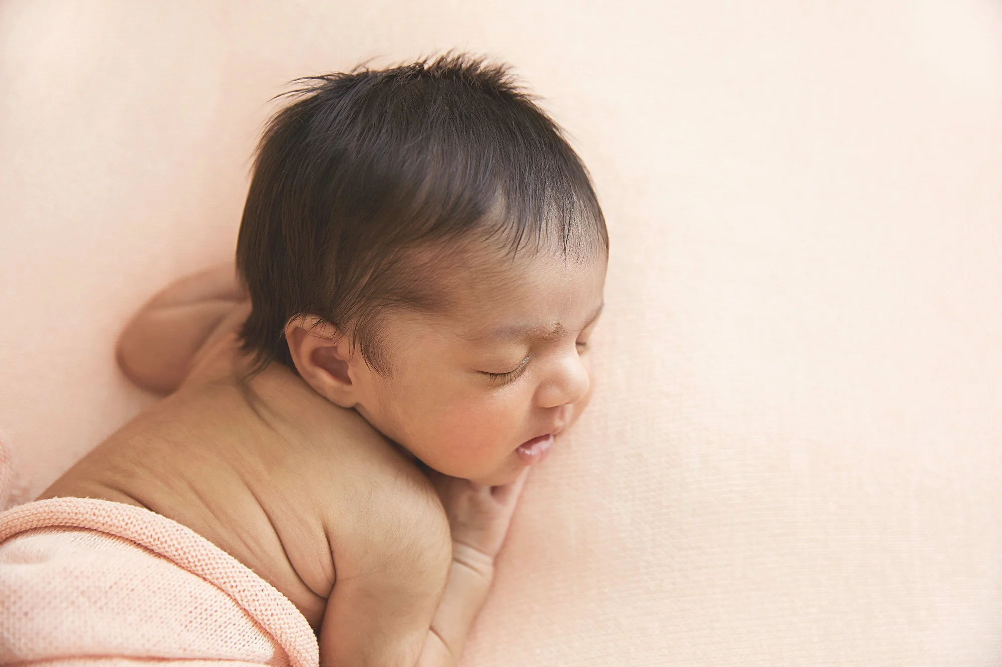 Close-up of a sleeping baby resting on a soft blanket against a light-colored background.