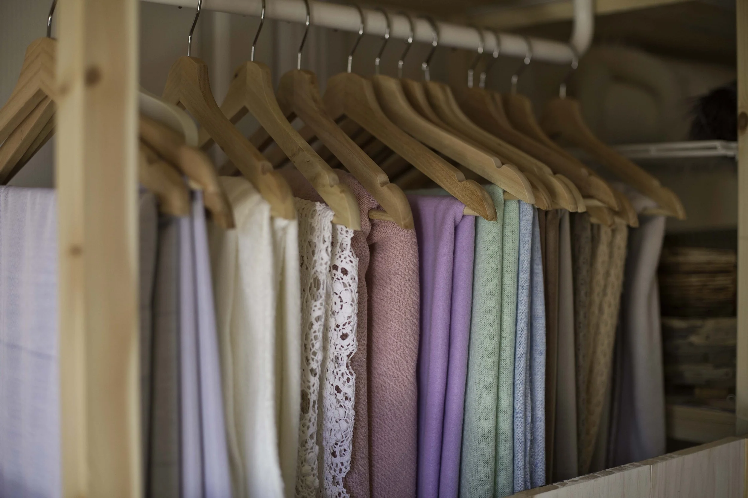A closet with a wooden rod holding several wooden hangers. The hangers are holding various backdrop fabric pieces for newborn photography in different colors.