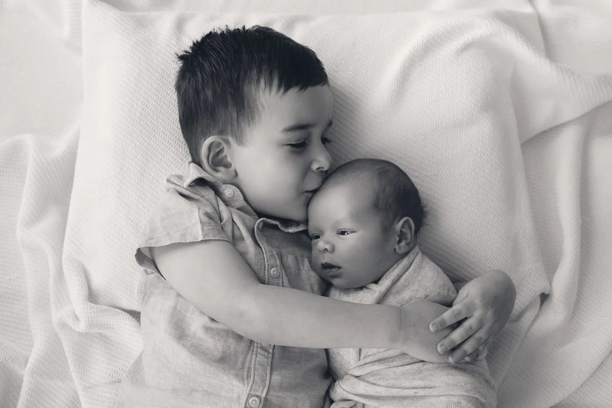 Sibling gently kissing newborn baby’s forehead during photo session.jpg