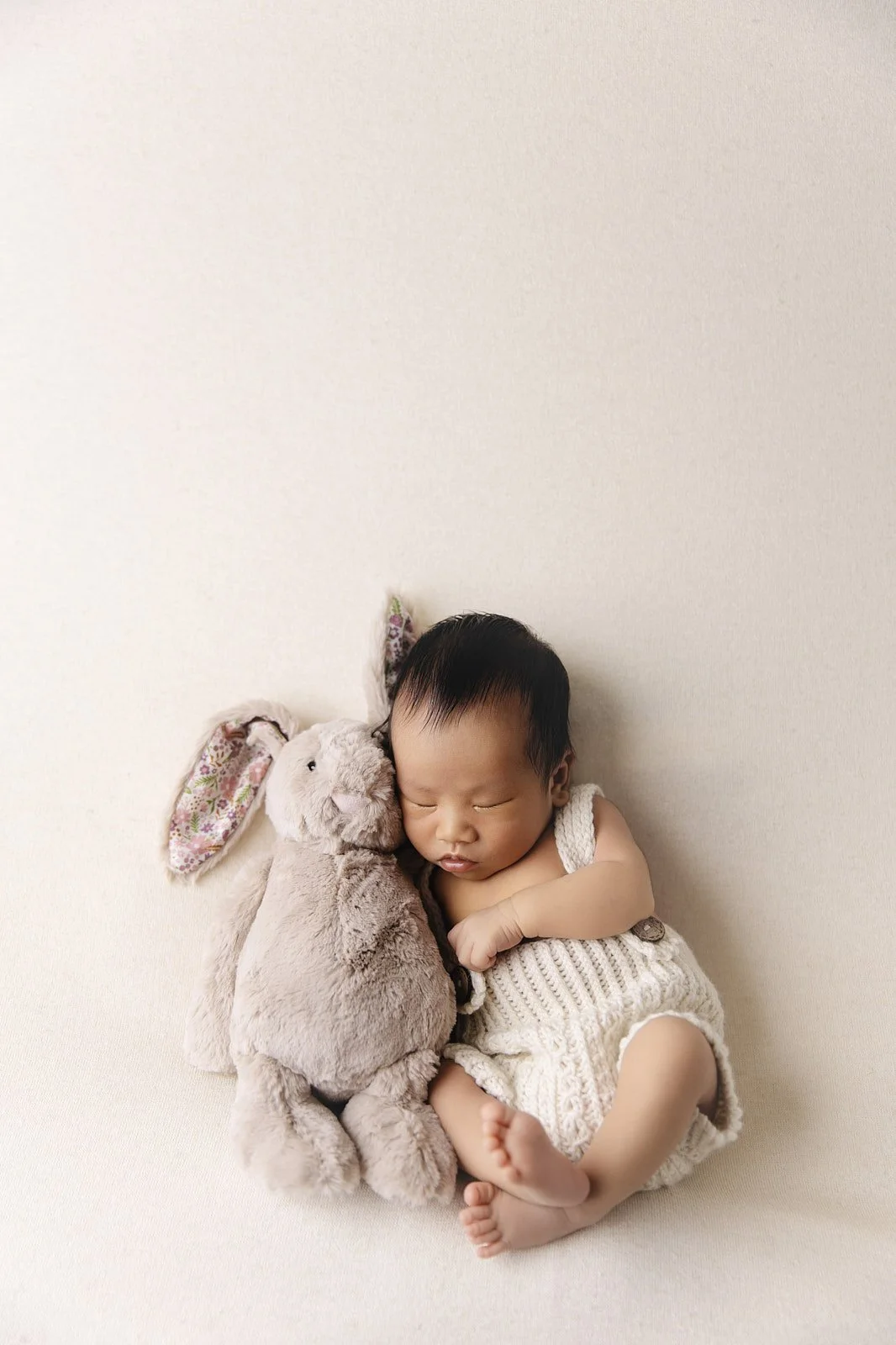 A sleeping baby hugging a plush bunny toy on a plain white background.