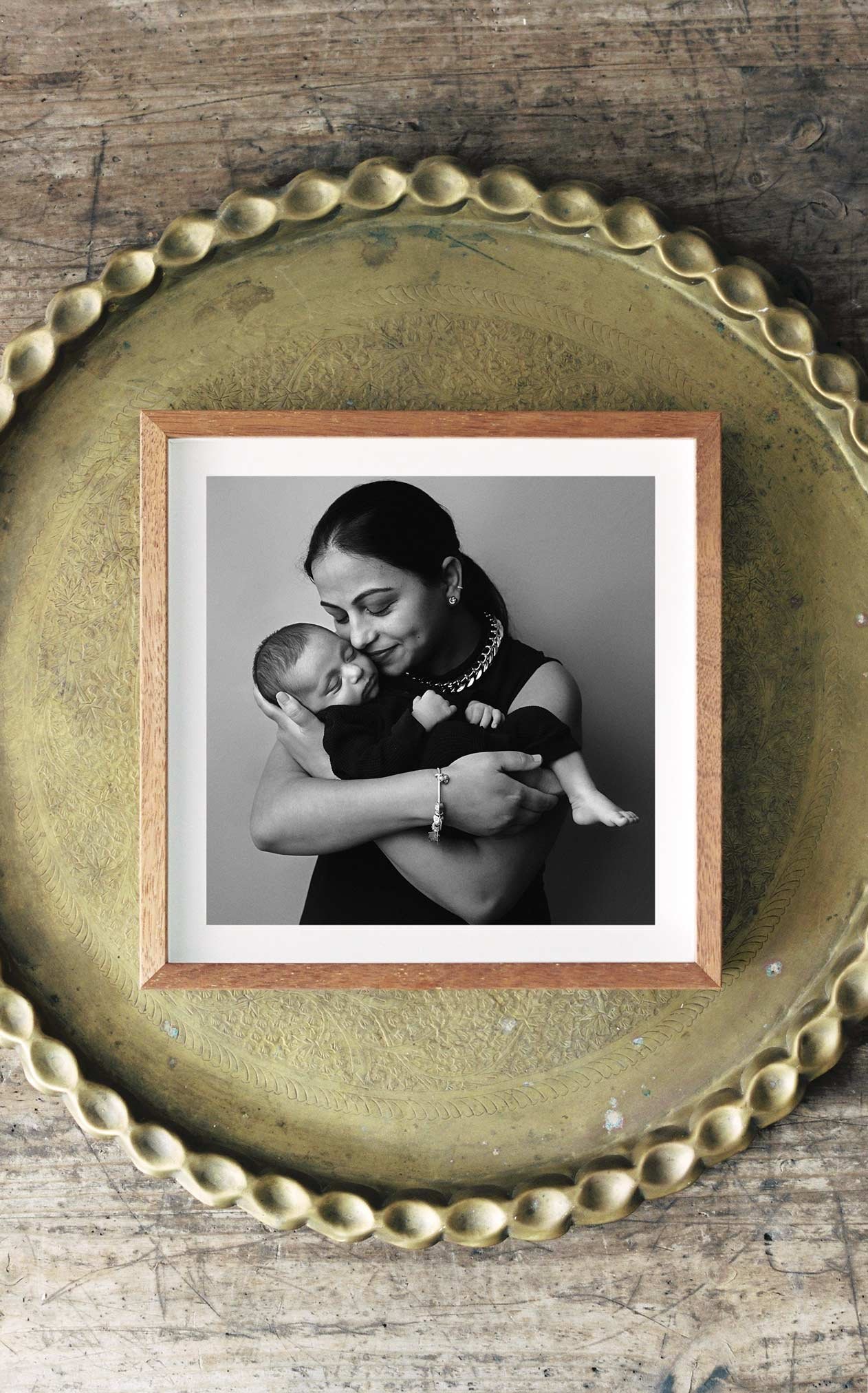 Black-and-white photo of a woman holding a sleeping baby, both smiling softly, inside a wooden frame on a decorative tray.