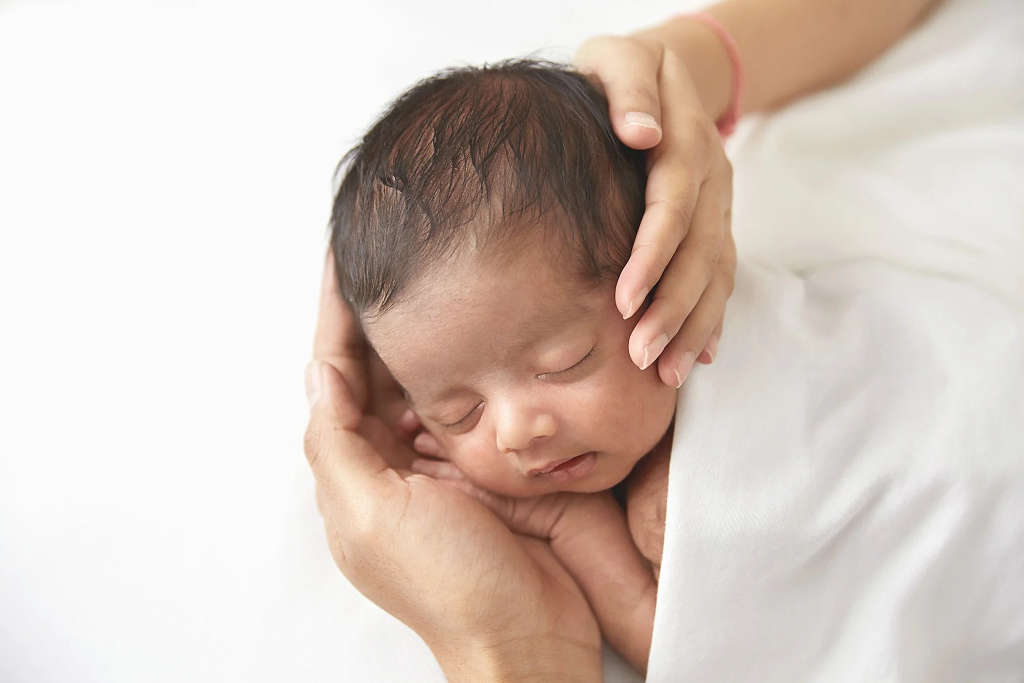 A newborn baby peacefully sleeping, cradled in a person's hands.