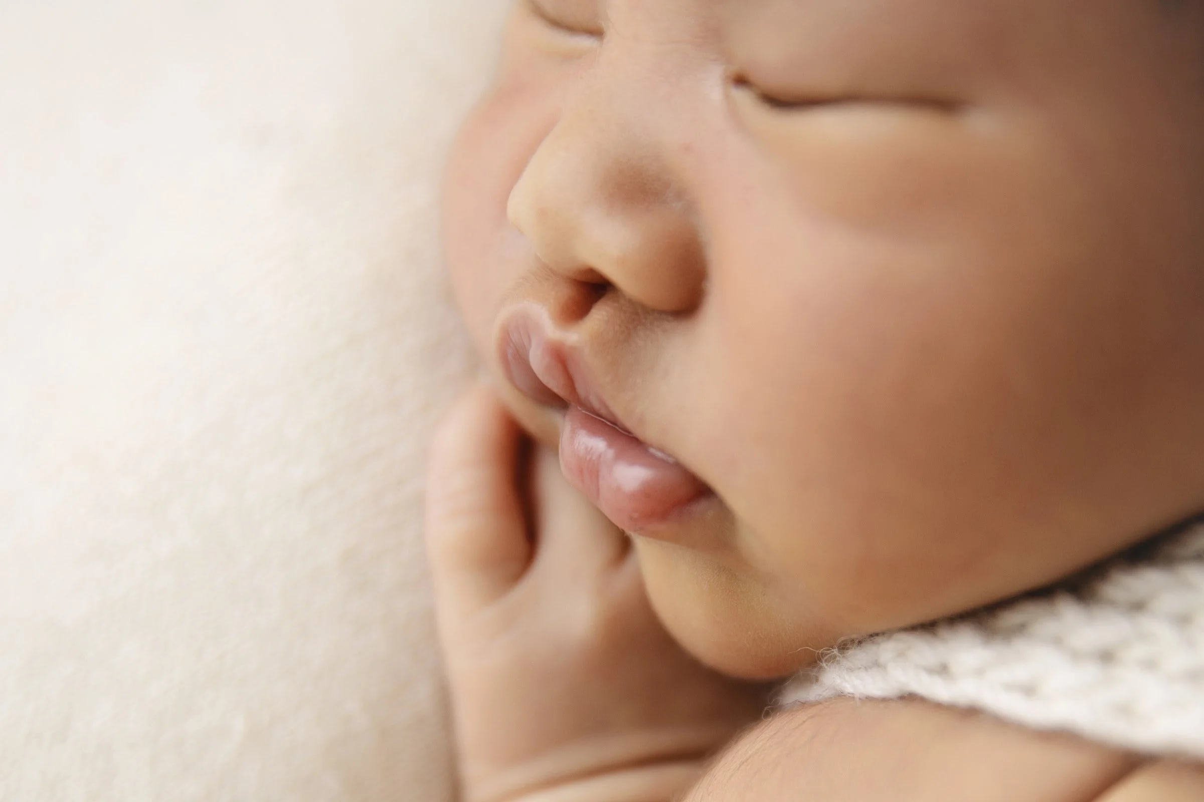 Close-up of a baby's face with eyes closed, nose, and lips, lying on a soft surface.