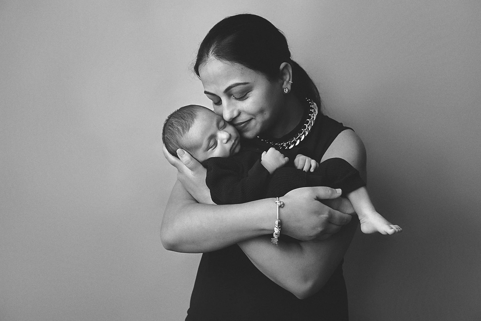 A woman holding a newborn baby close to her face, both with eyes closed, sharing a tender moment.