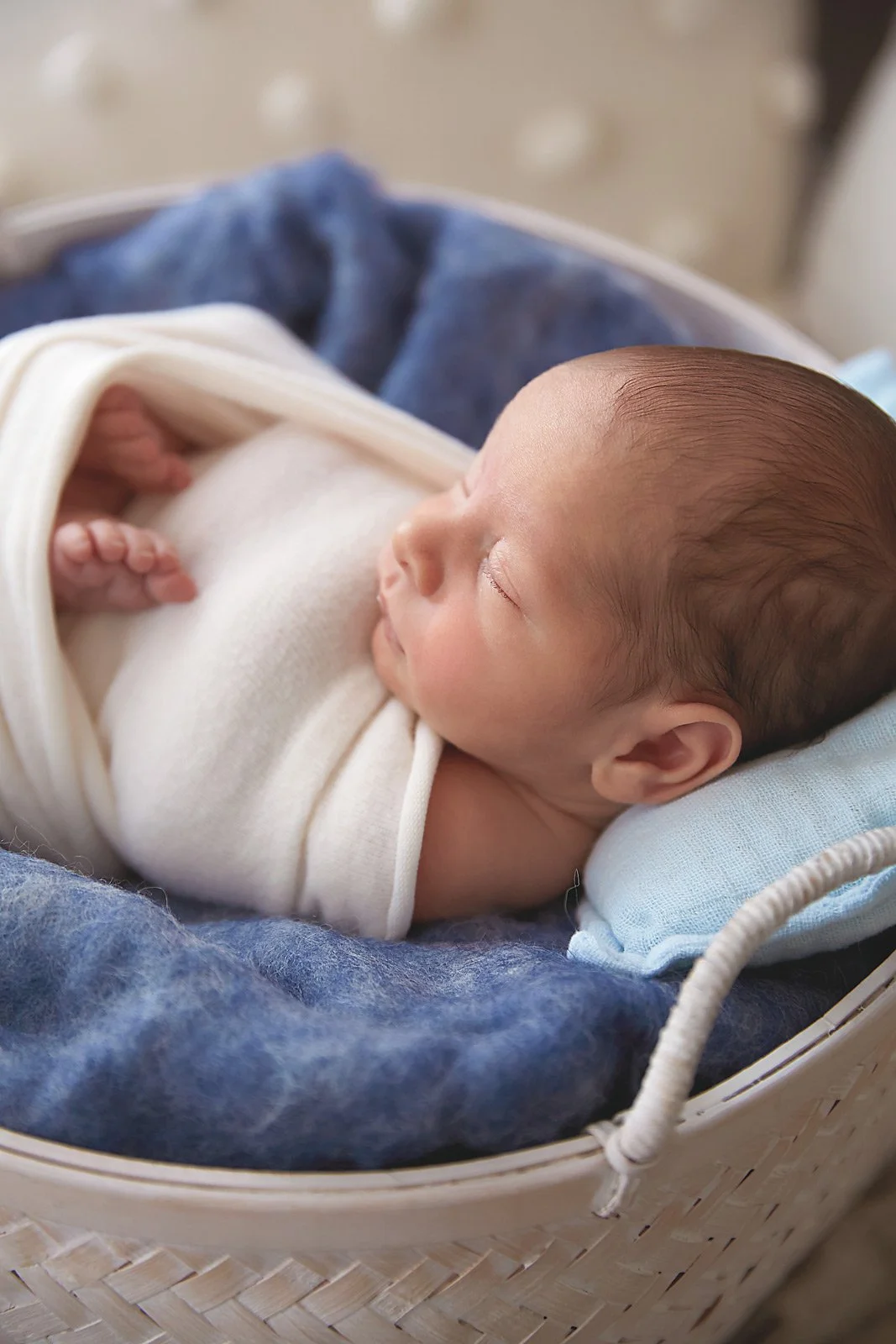 A sleeping infant lying in a woven basket on a soft blanket, wrapped in a white cloth.