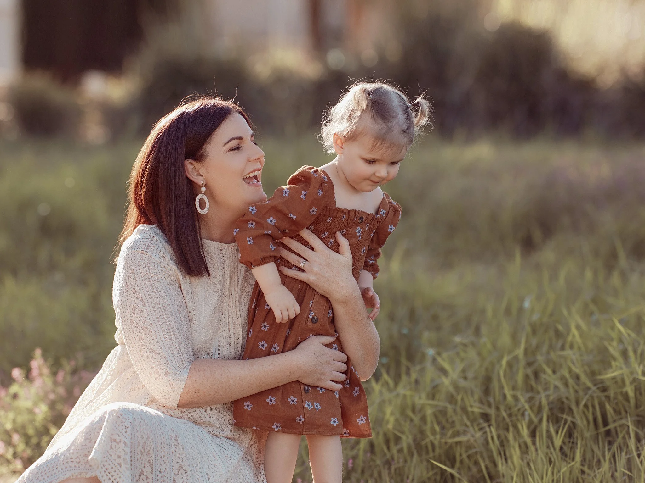 A woman holding a young girl outdoors in a grassy field during sunset.