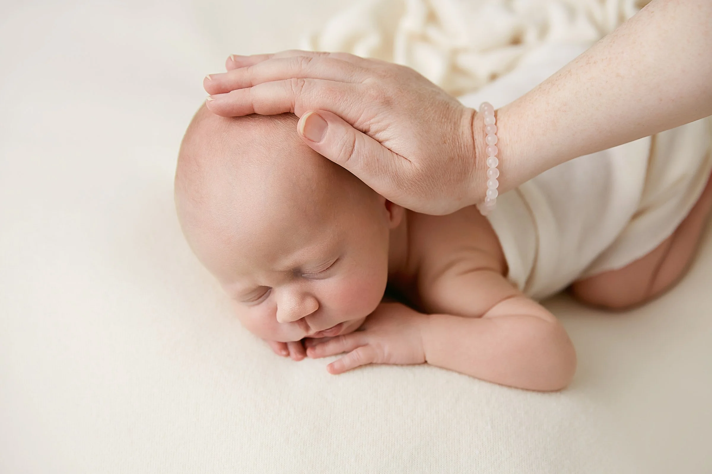 Minimalist and warm newborn baby photography in Sydney featuring a mother’s hands on a sleeping baby to show a gentle, patient approach