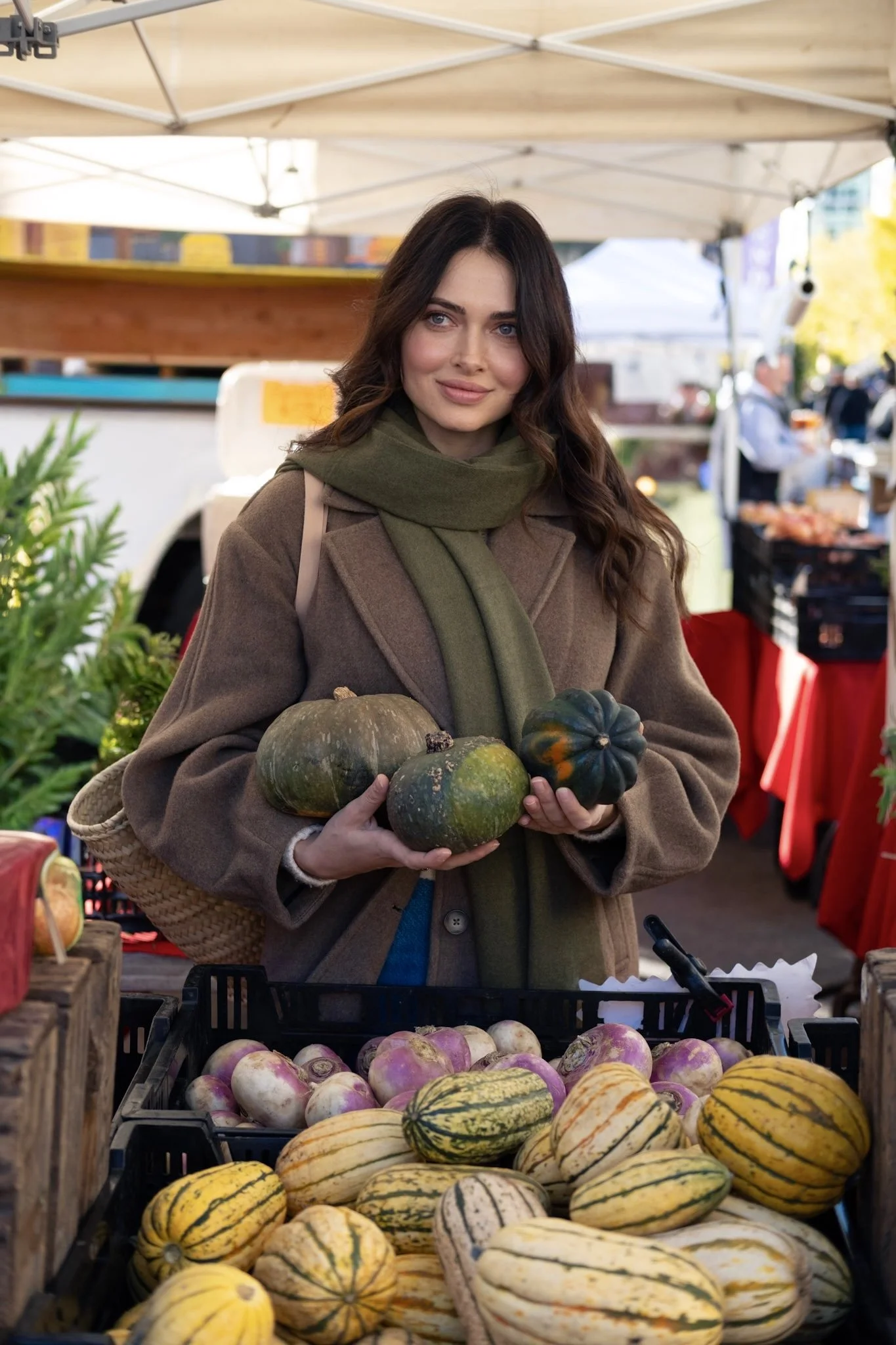 Woman shopping for squash and pumpkins at an outdoor farmers market.