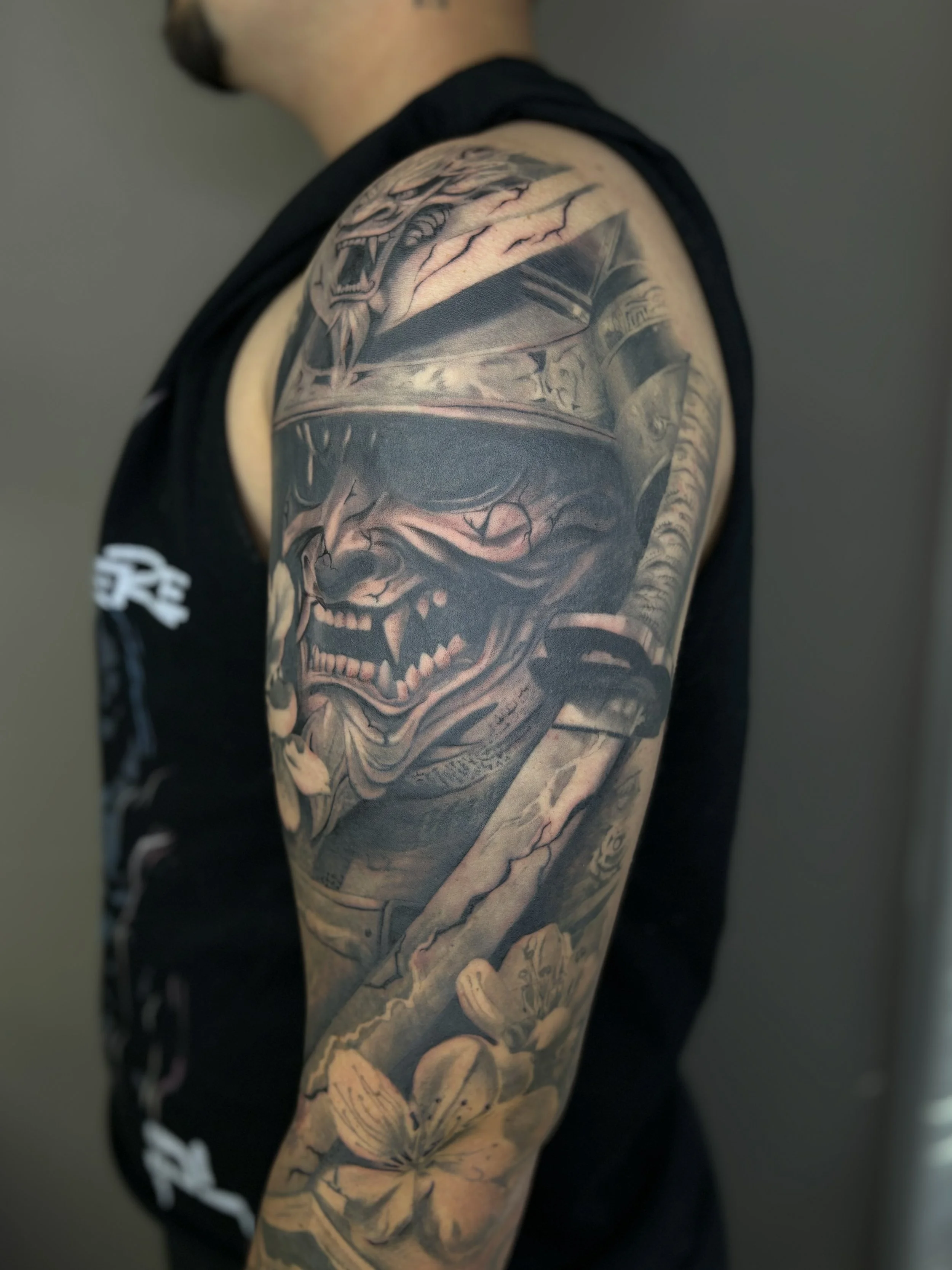 Black and gray tattoo sleeve featuring a fierce snarling wolf wearing a helmet, with a sword and a flower below, on a person's upper arm.