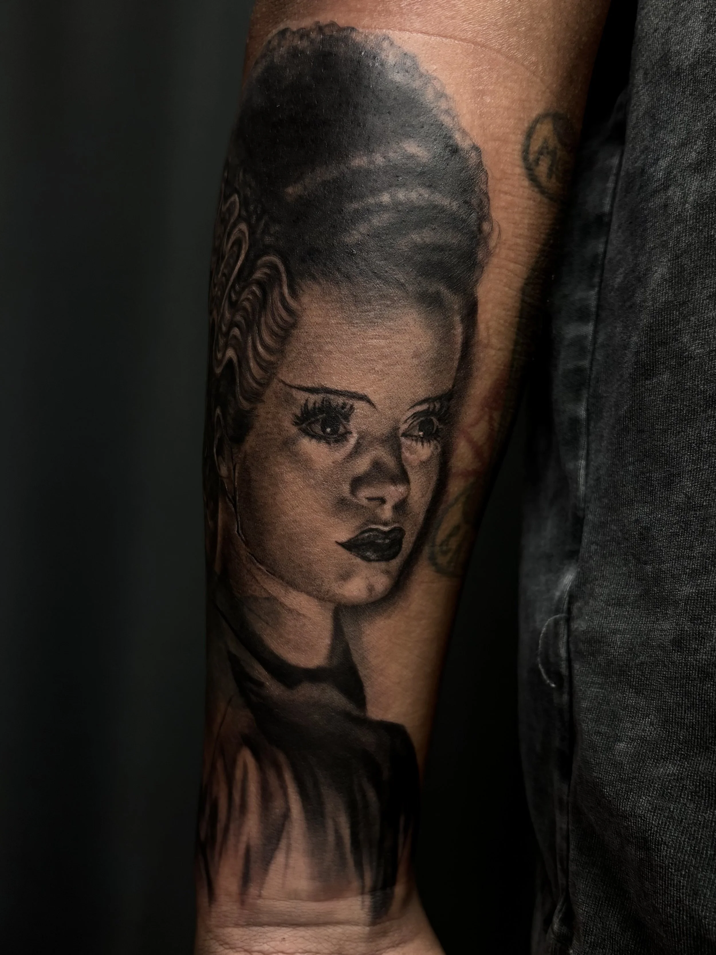 Black and gray tattoo of a woman's face with detailed hair and makeup on an arm.