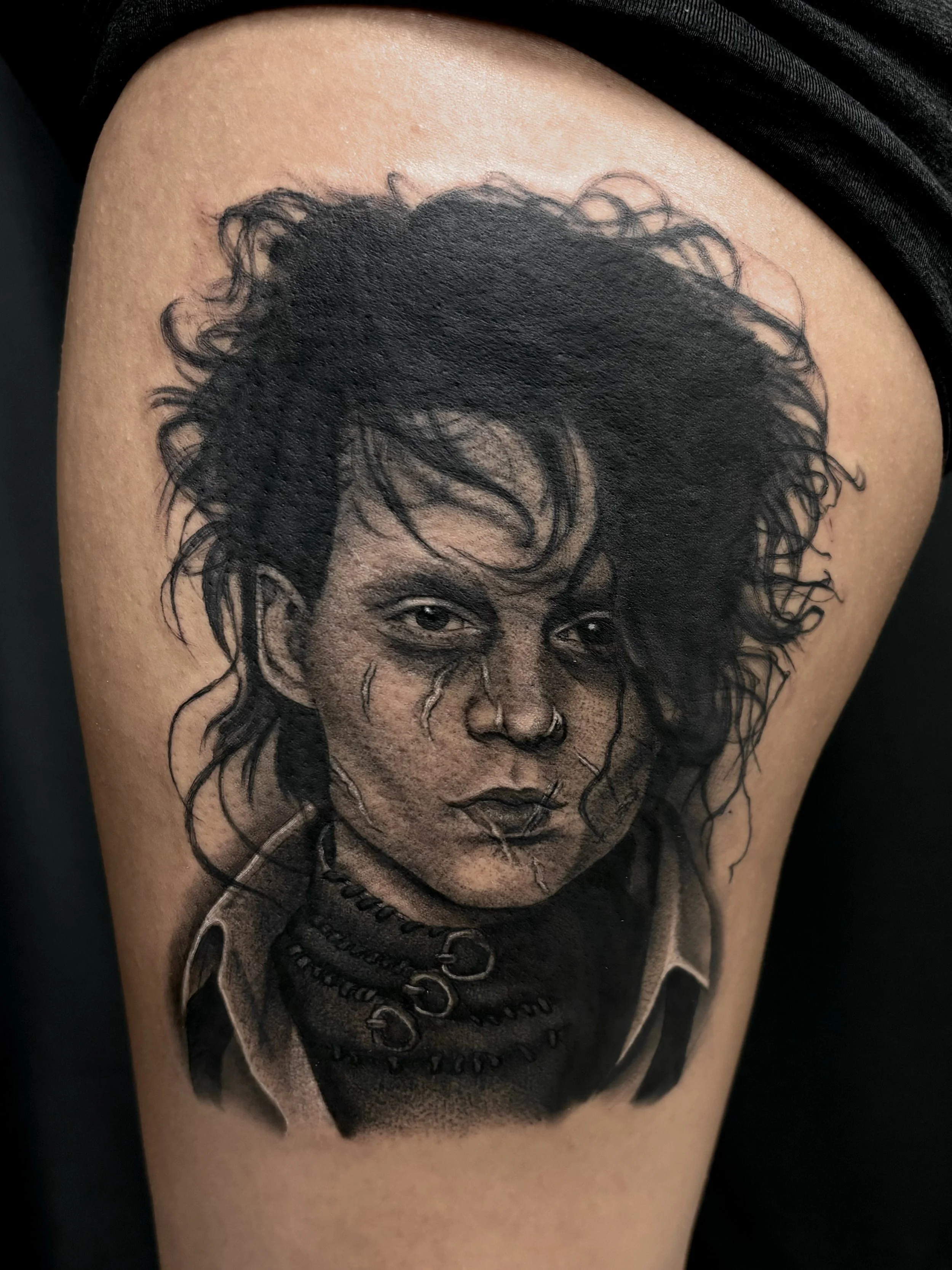 Black and grey realistic tattoo of a person with messy, curly hair, facial scars, and dark clothing, on person's upper arm.