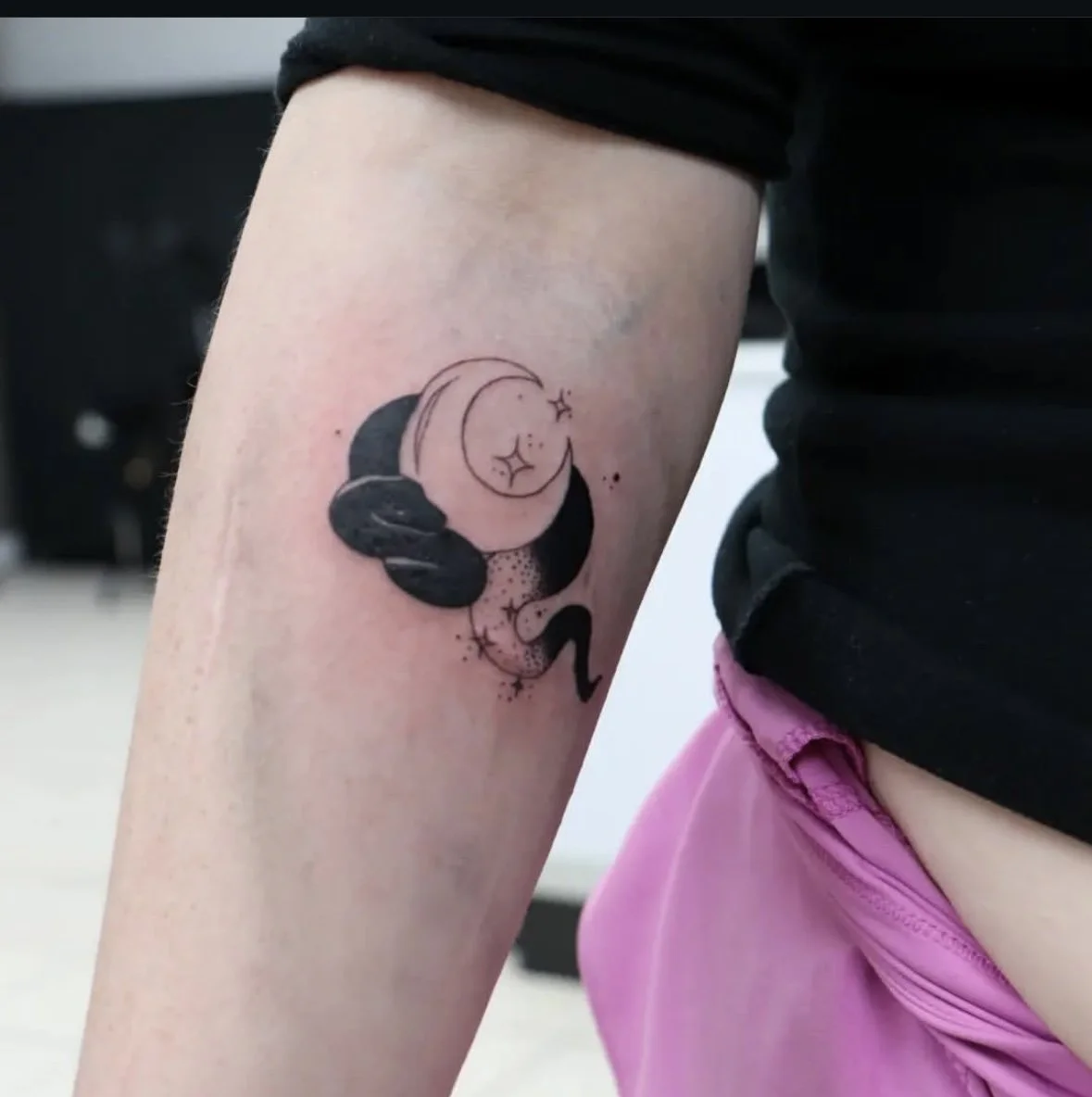 Tattoo on person's arm featuring a crescent moon, a smaller moon with stars, and black clouds, with a galaxy-like design.