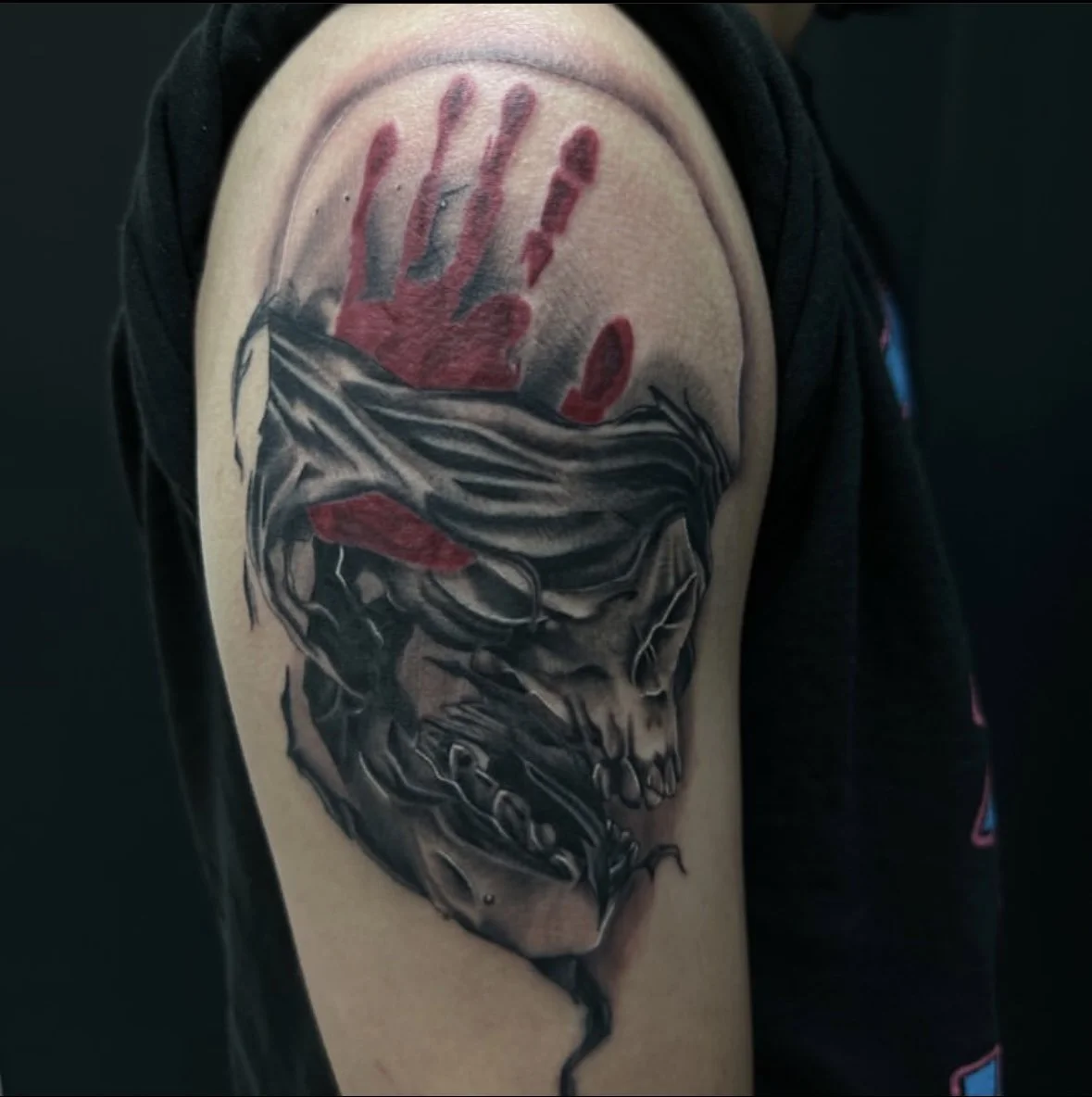 Tattoo of a skull with a handprint above it and a red lipstick mark.