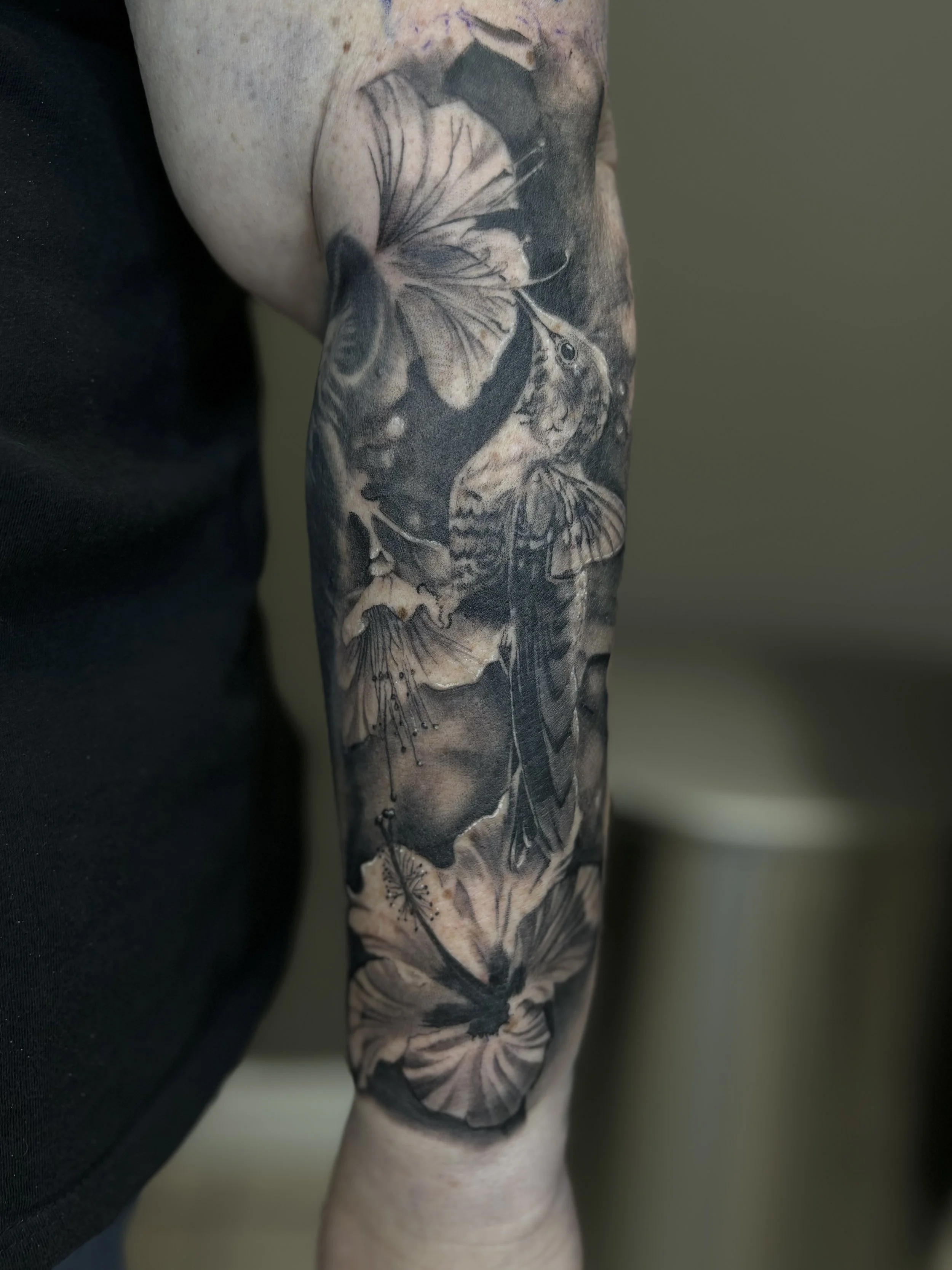 Black and gray tattoo sleeve featuring large realistic butterflies and floral elements on a person's arm.