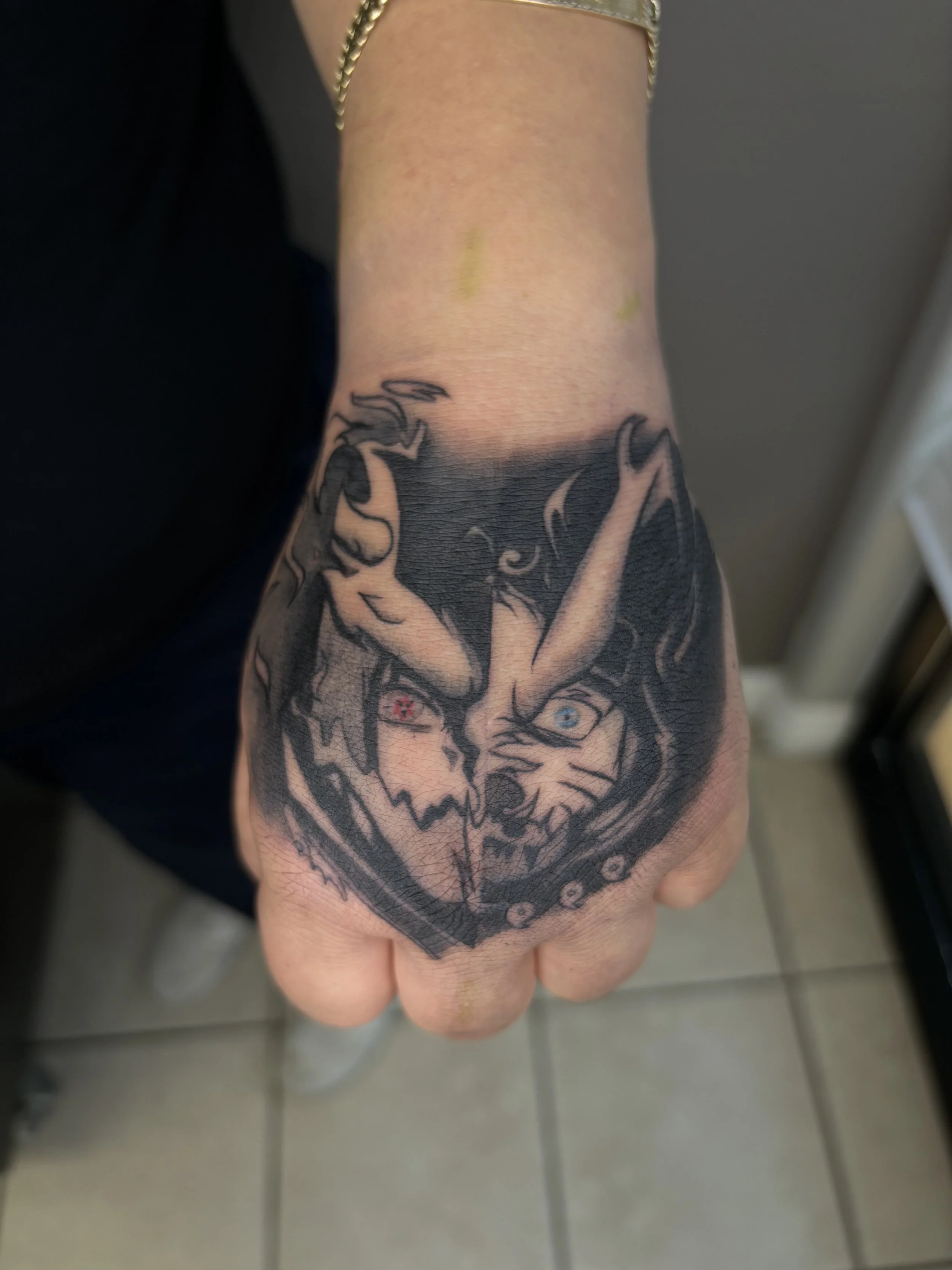 Tattoo of a fierce animal face with two eyes, one red and one blue, on a person's hand.