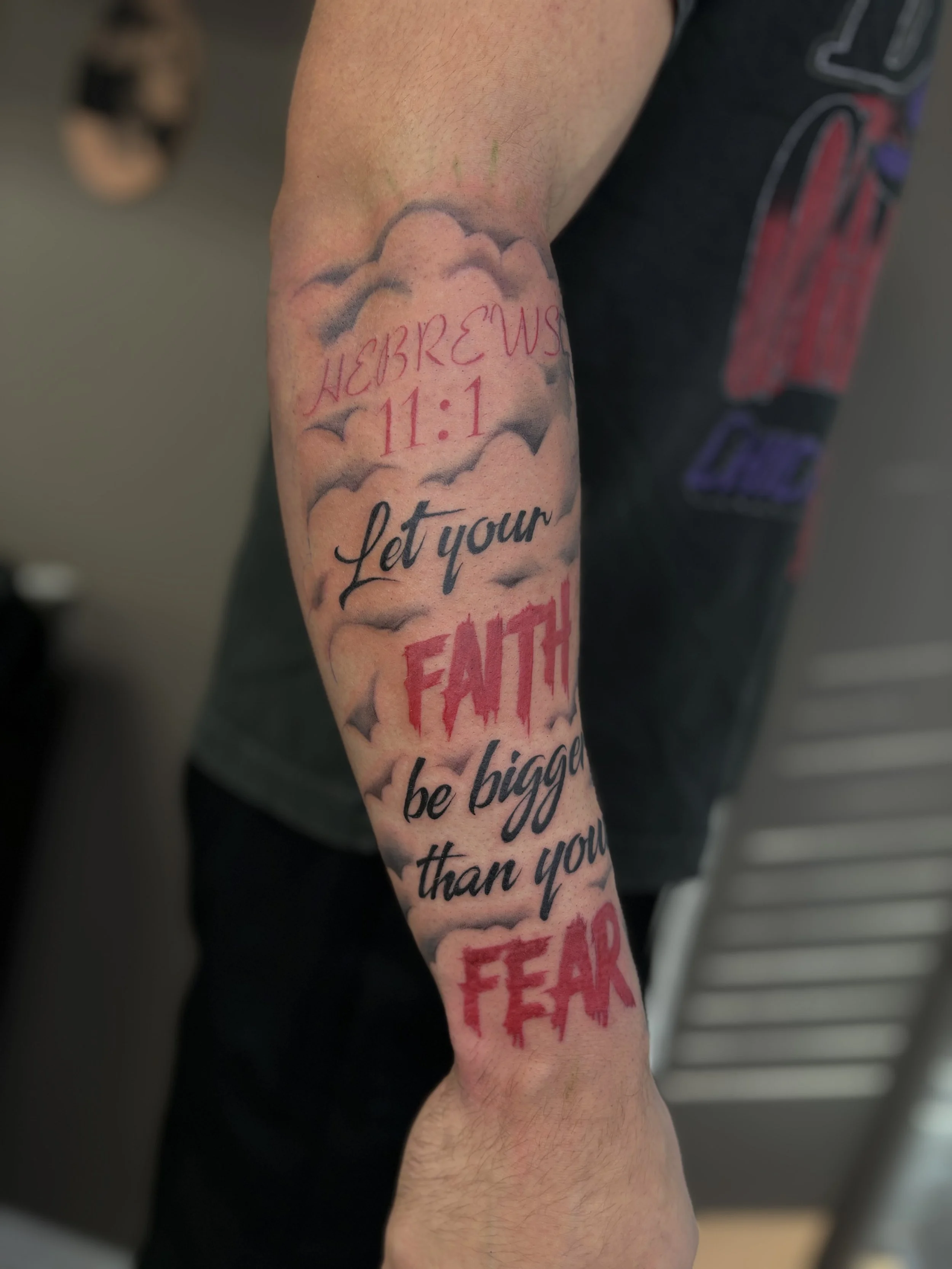 Tattoo sleeve with clouds, the words 'Hebrews 11:1', and a motivational phrase 'Let your faith be bigger than your fear' on a person's arm.