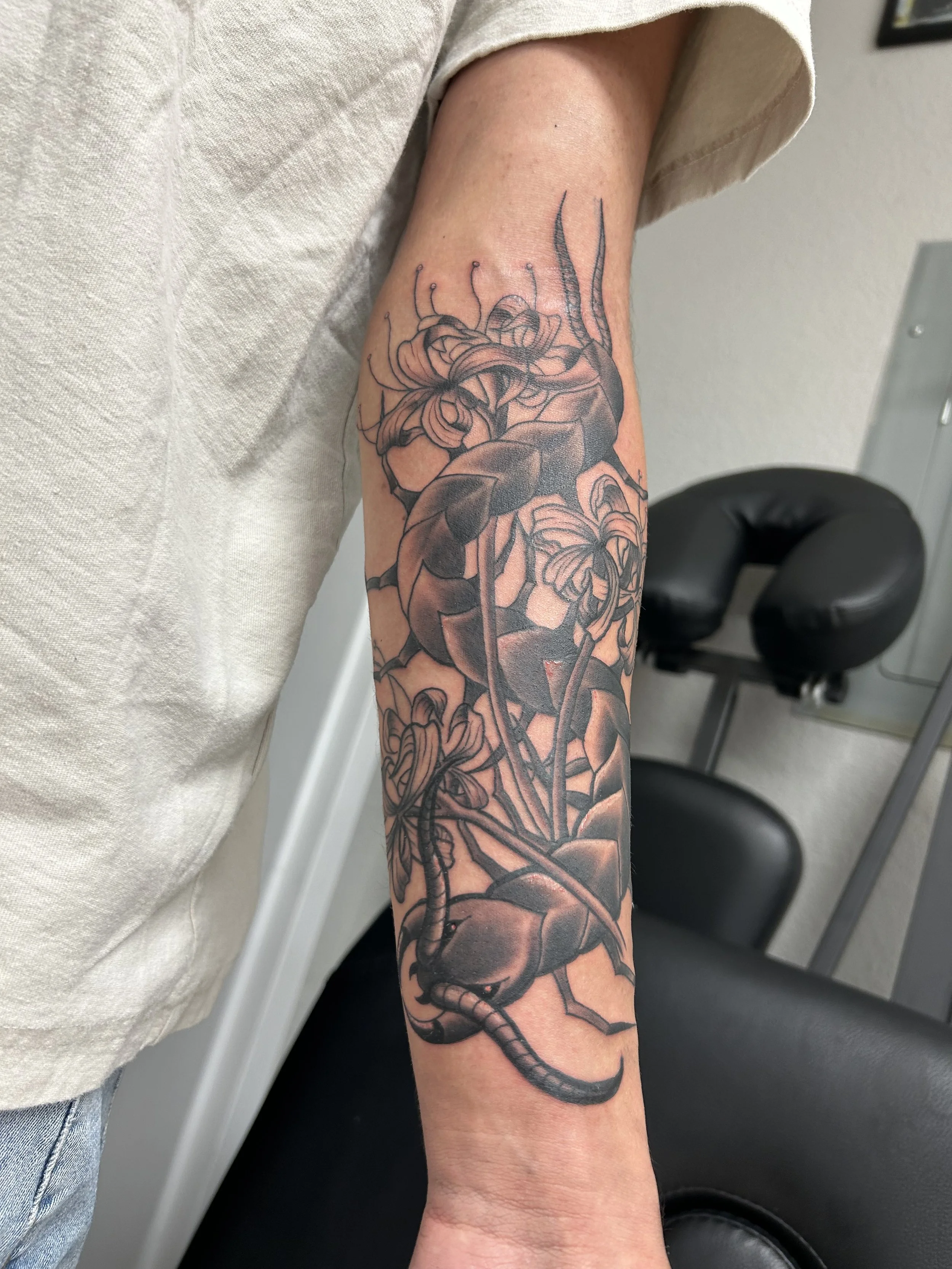 Black and gray tattoo of a scorpion and flowers on a person's forearm.