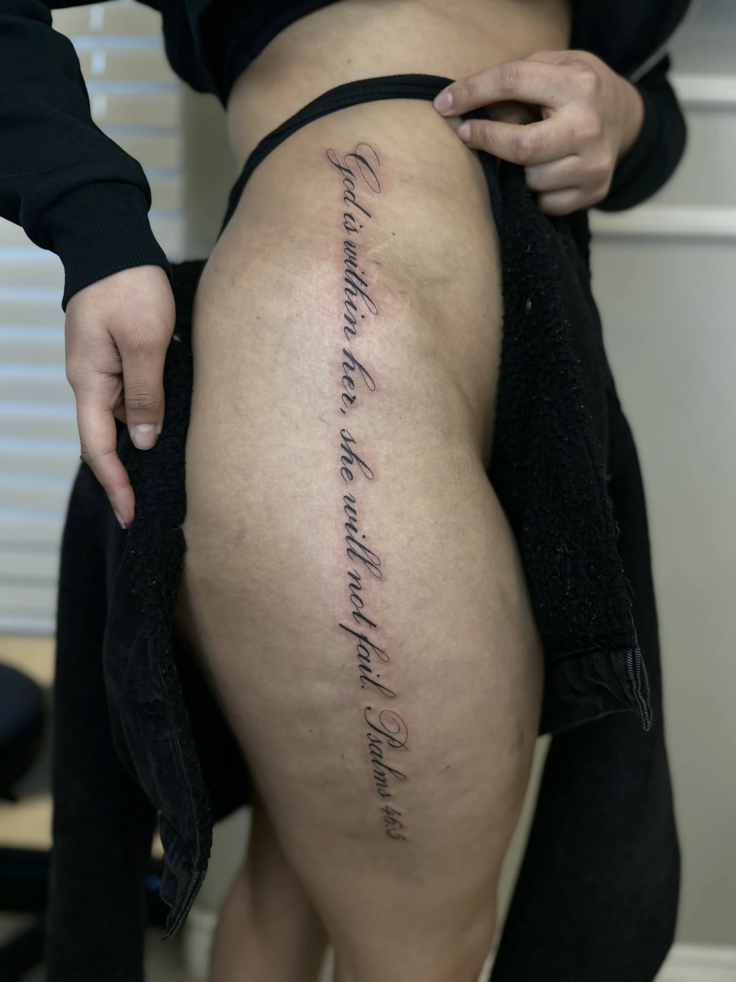 A person showing a thigh tattoo with a quote written in cursive script.