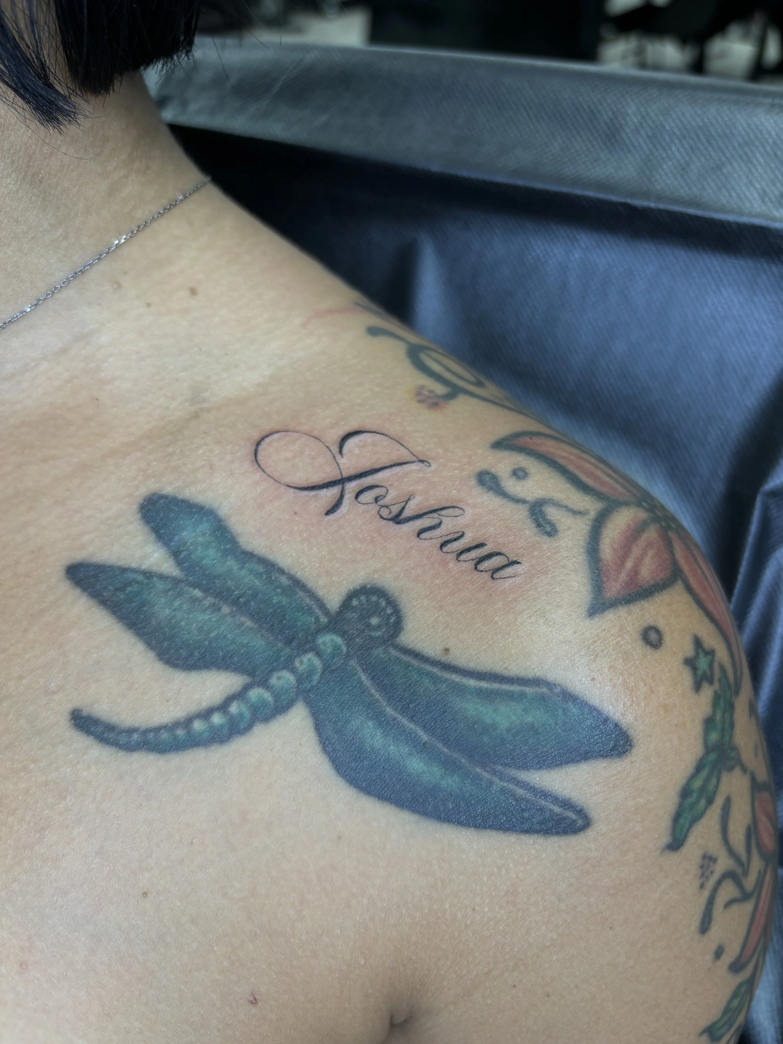 Tattoo of a dragonfly and the name Tashlea on a person's shoulder.