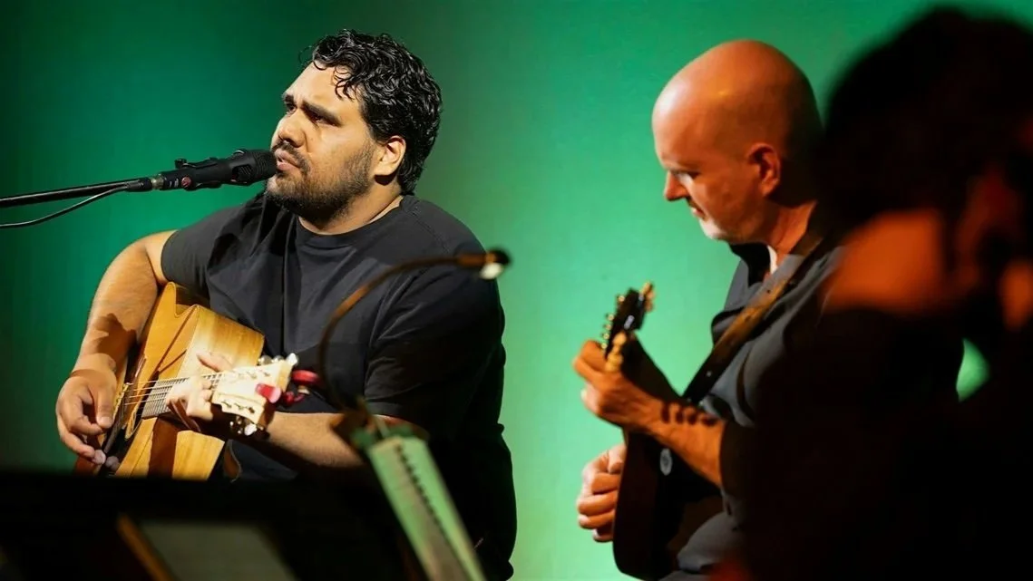 Two musicians performing together, playing guitars and singing into a microphone.