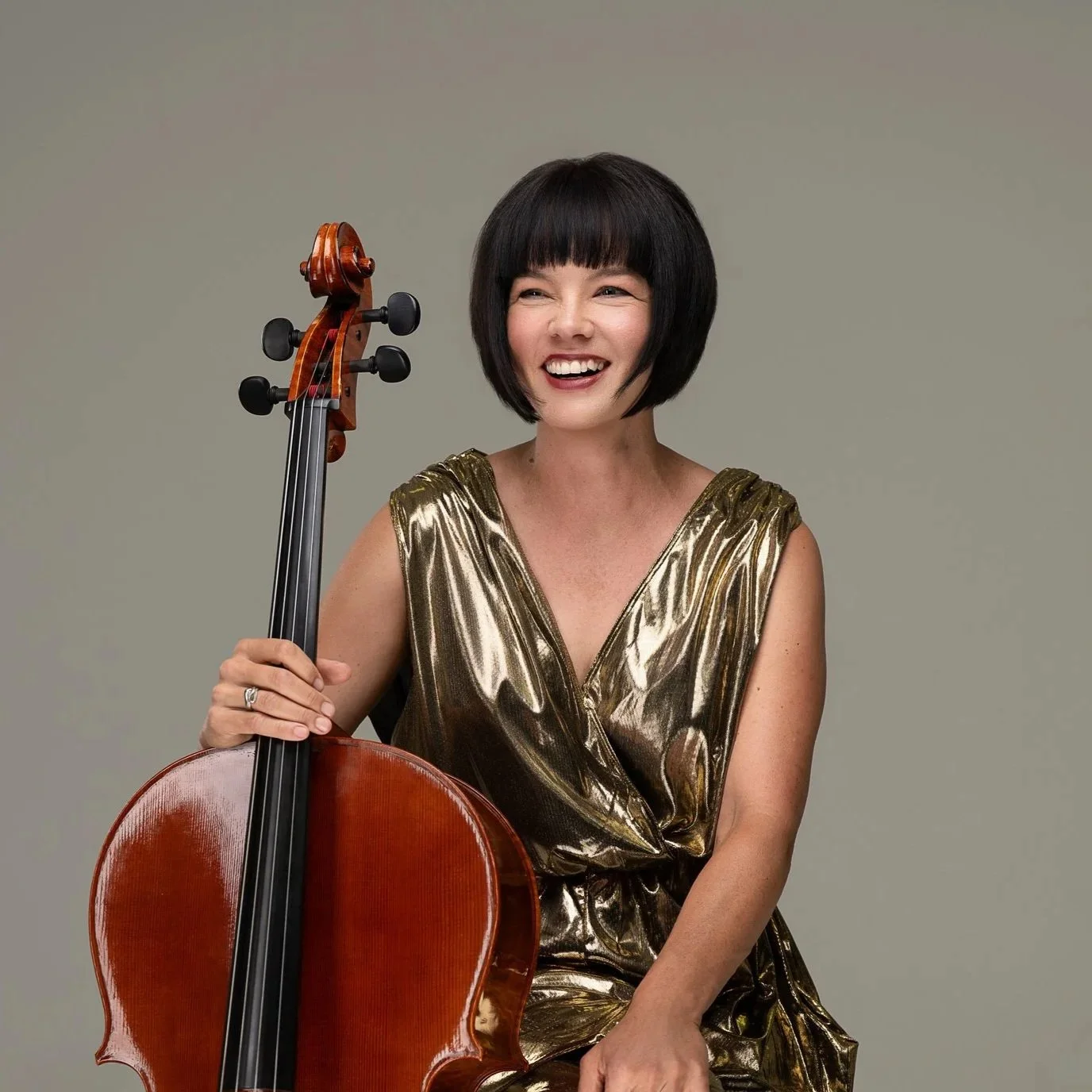 A photo by Sam Oster showing Hilary Kleinig seated in a gold dress, holding a cello.