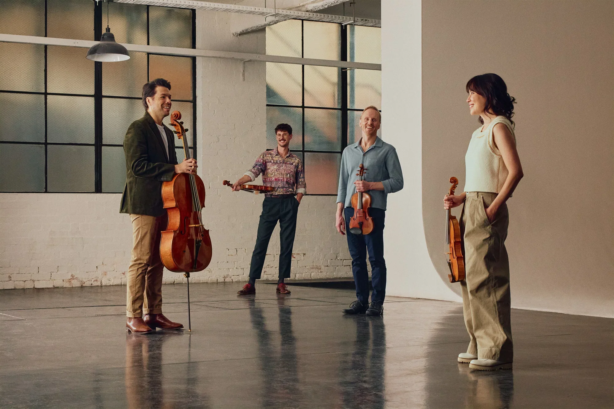 A string quartet in casual dress holding their instruments. They stand in a sparse warehouse space, giving the image an industrial look.