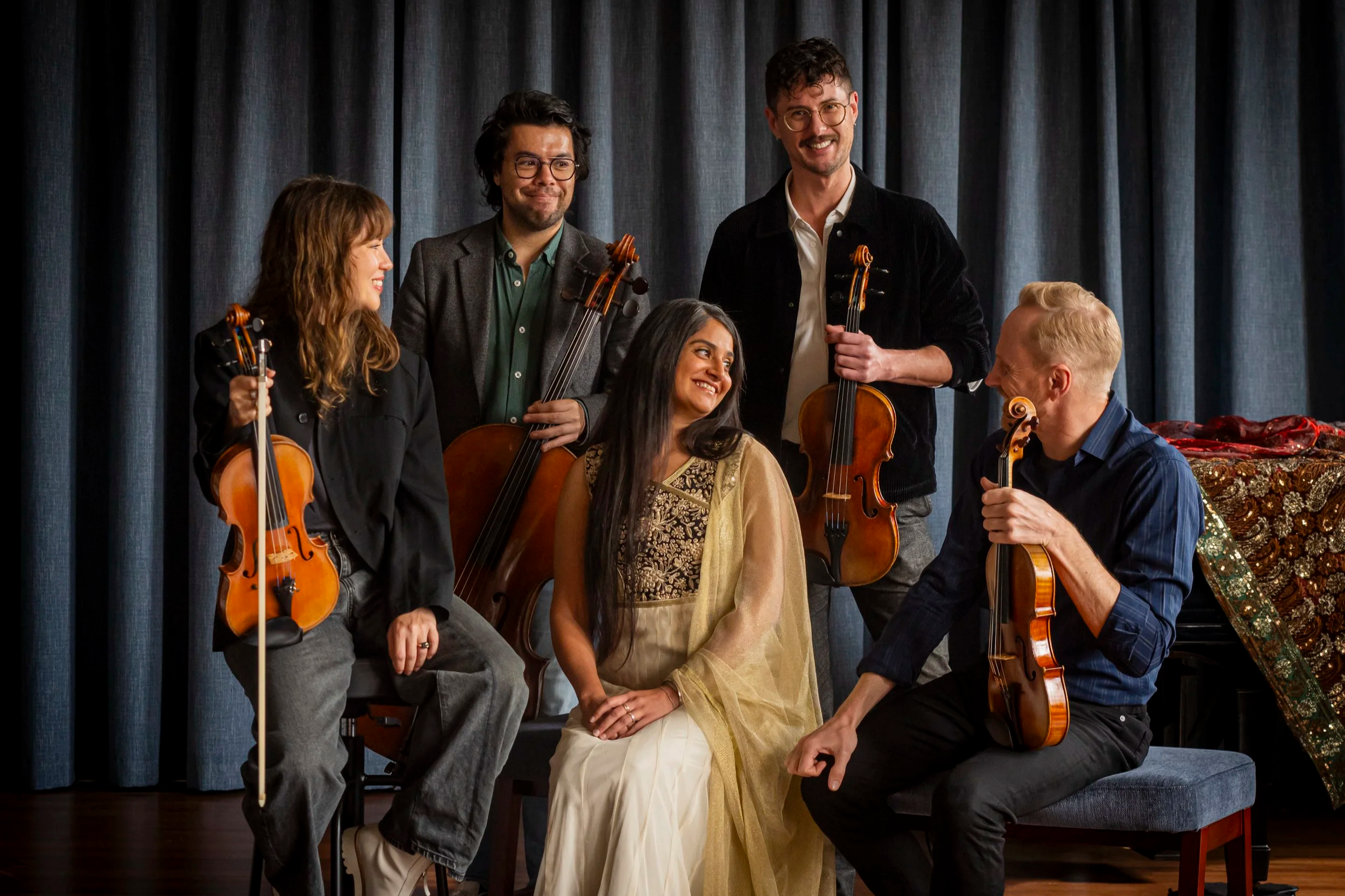 Australian String Quartet are gathered around vocalist Parvyn, who is seated. A piano and blue drapes create a backdrop for the group portrait.