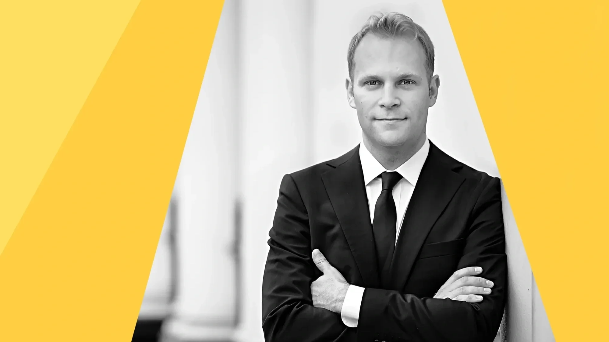 A black and white photo of a person in a suit with arms folded, looking directly at the camera. There are overlayed graphic panels in shades of yellow.