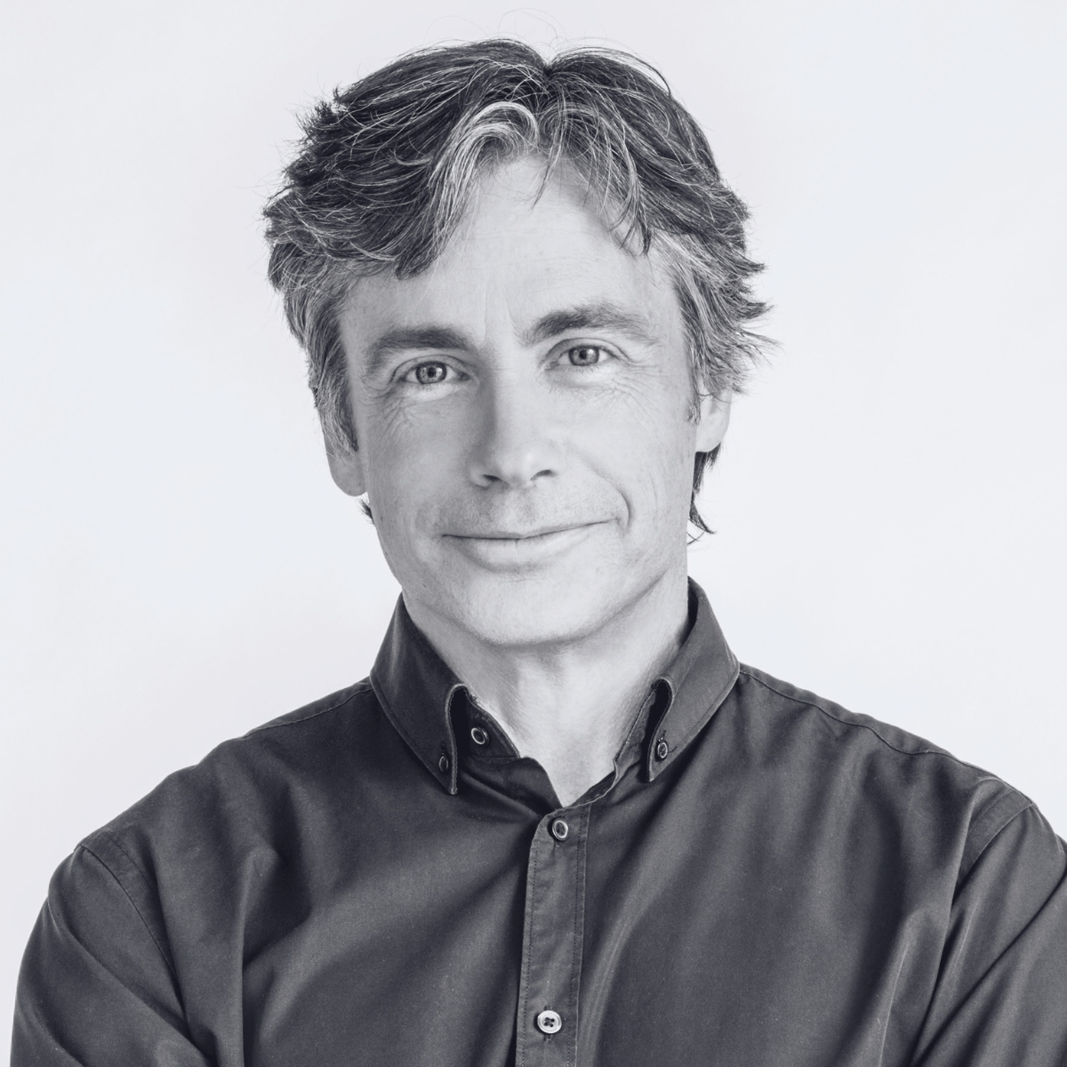 A black and white photo of a man wearing a dark shirt. He looks directly at the camera with a gentle smile.