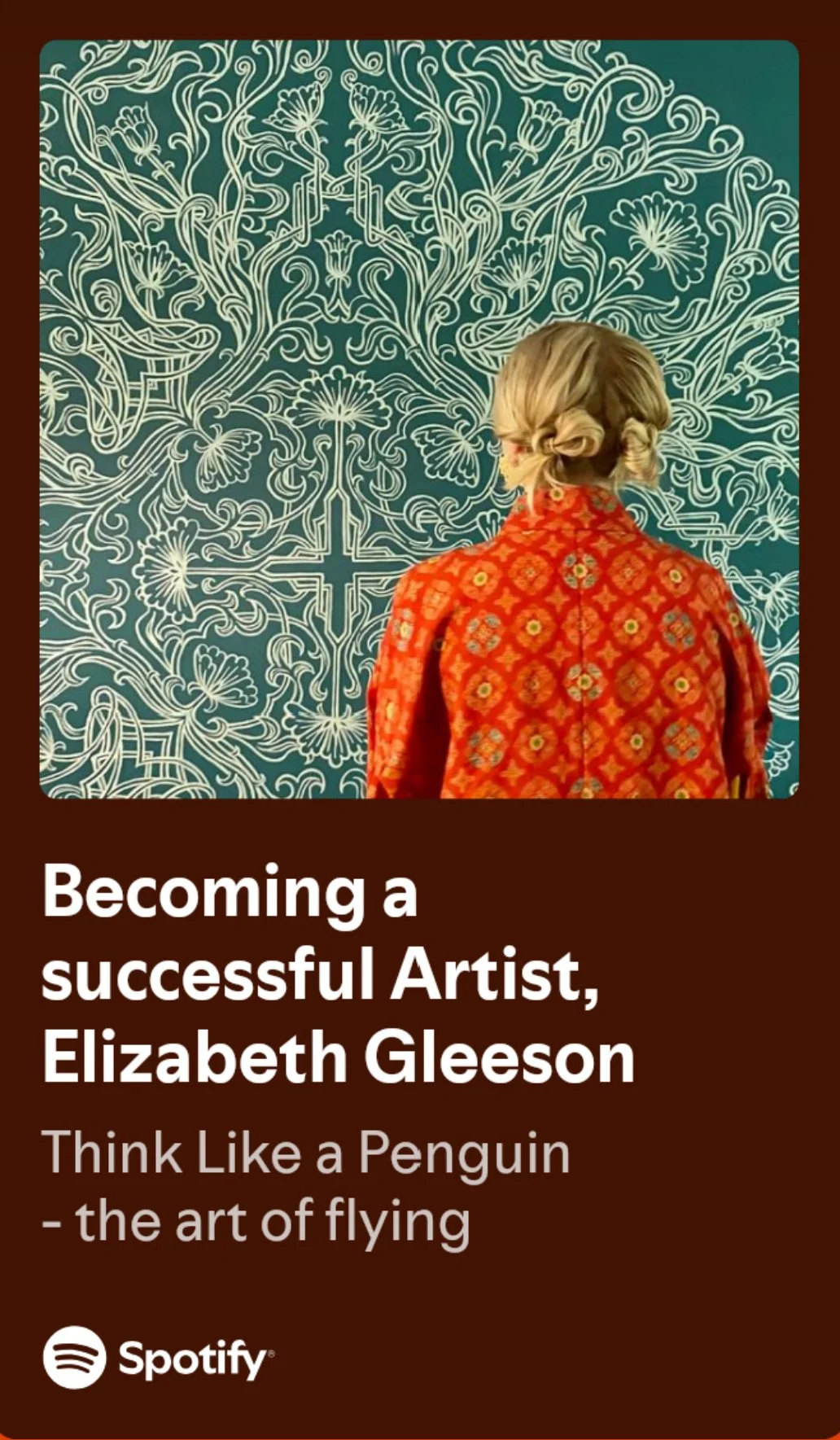 A woman with blonde hair styled in a braided bun, wearing a red patterned jacket, stands in front of an intricate white line drawing of plants and flowers on a blue background.