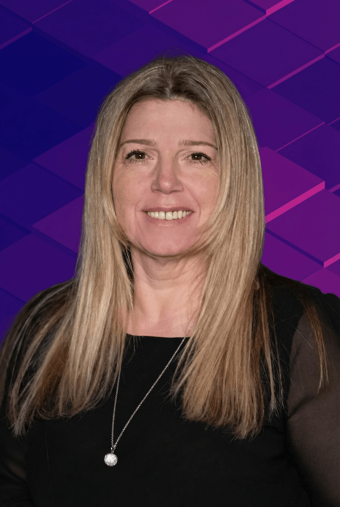 Ein Lächelndes Frau mit langen blonden Haaren, trägt eine schwarze Bluse und eine Halskette mit einem runden Anhänger.