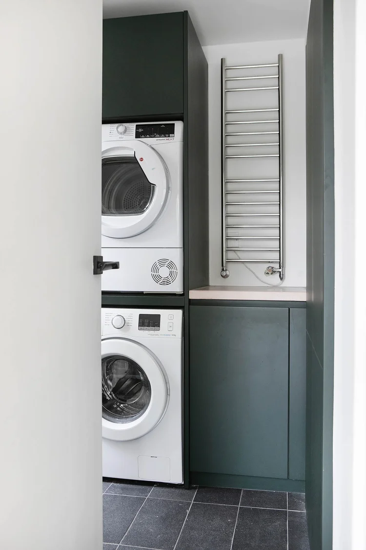 Tall utility housing with washing machine and dryer stacked behind a door.