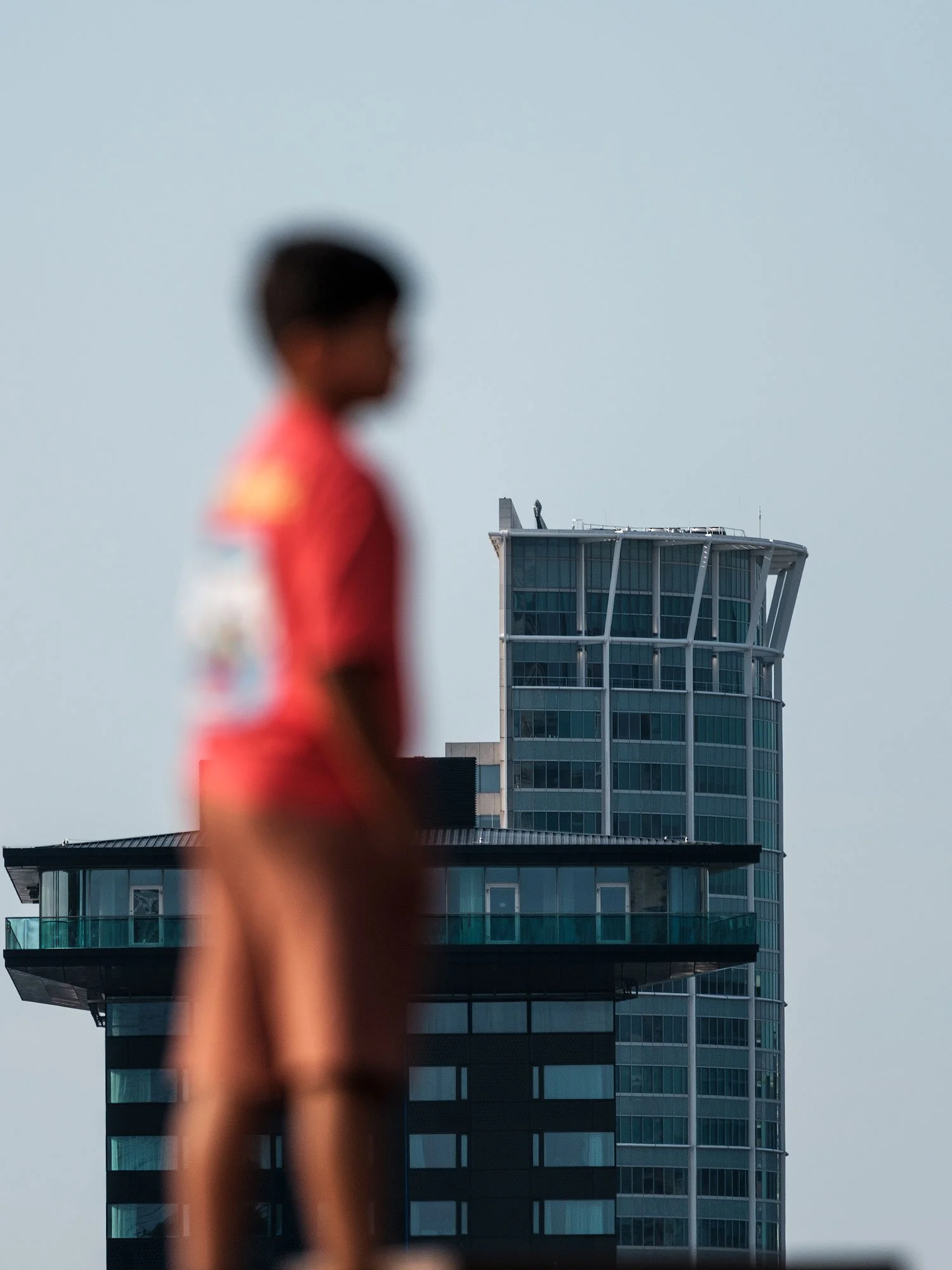 Out-of-focus person in red crossing the foreground with a modern Rotterdam tower in focus behind.