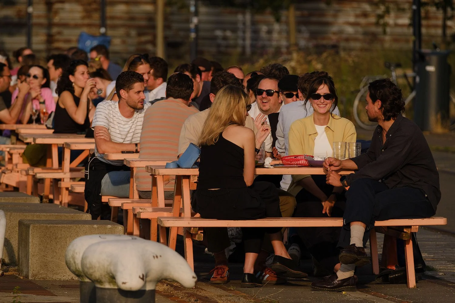 People socialising at outdoor picnic tables on a Rotterdam terrace in warm evening light.